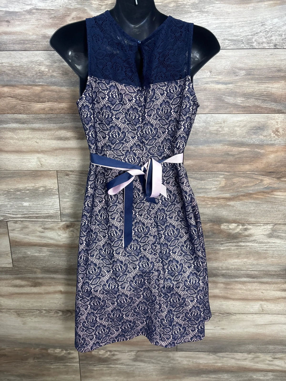 Front view of navy maternity lace dress with sleeveless lace bodice and navy and pink ribbon belt on wooden backdrop