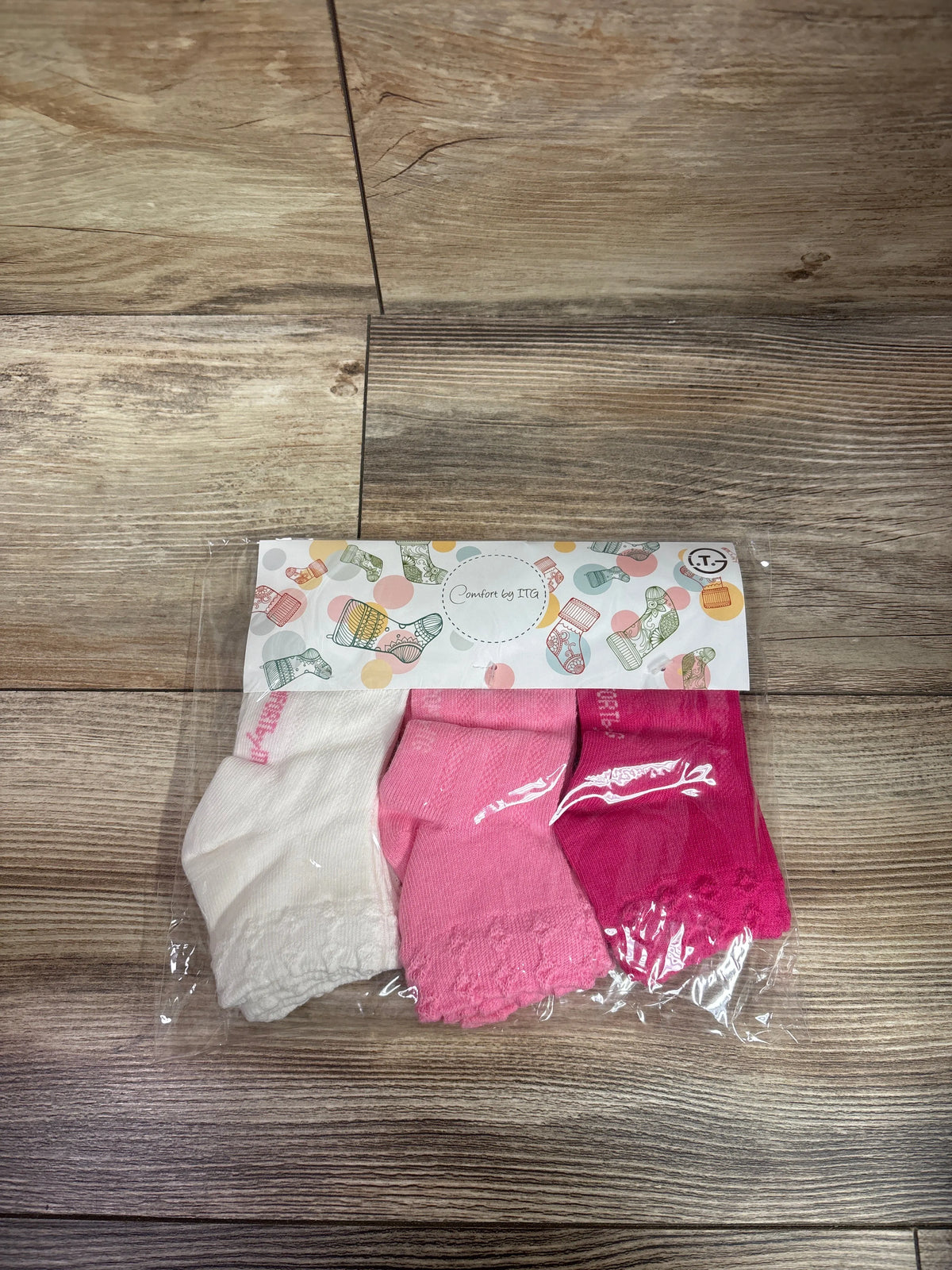 Front view of Comfort by ITG girls socks six pack showcasing white and pink socks in clear packaging on a wood surface