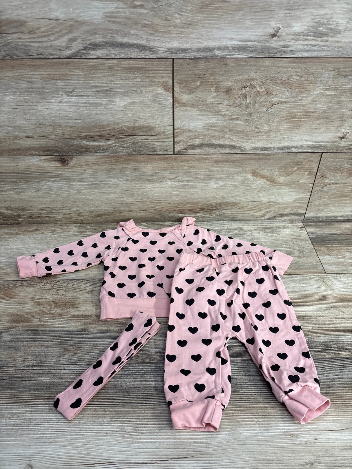 Pink baby outfit with black heart prints including top, pants, and matching headband on wooden floor
