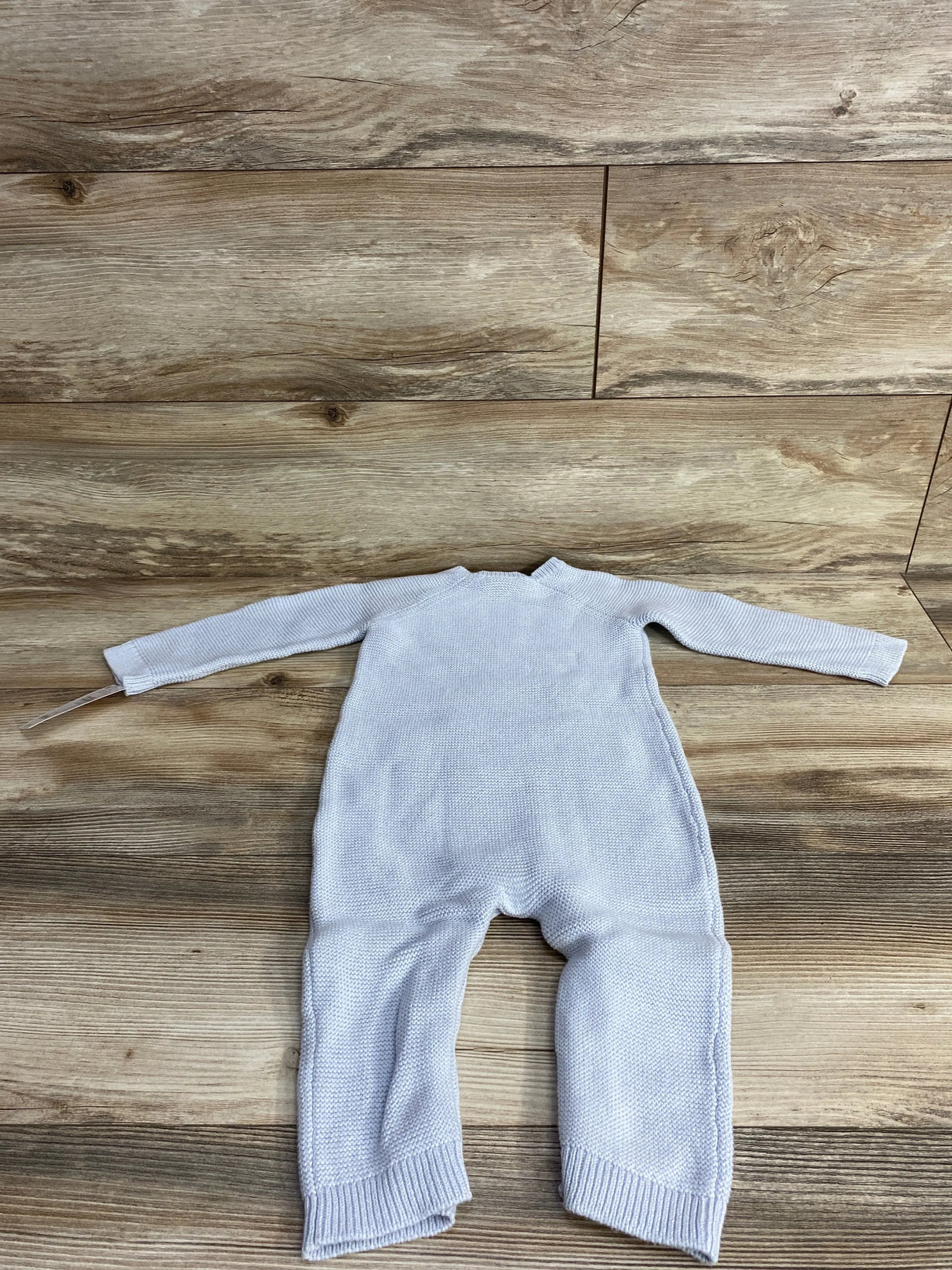 Back view of light blue chunky knit sweater coverall with ribbed cuffs and full-length legs on wood background