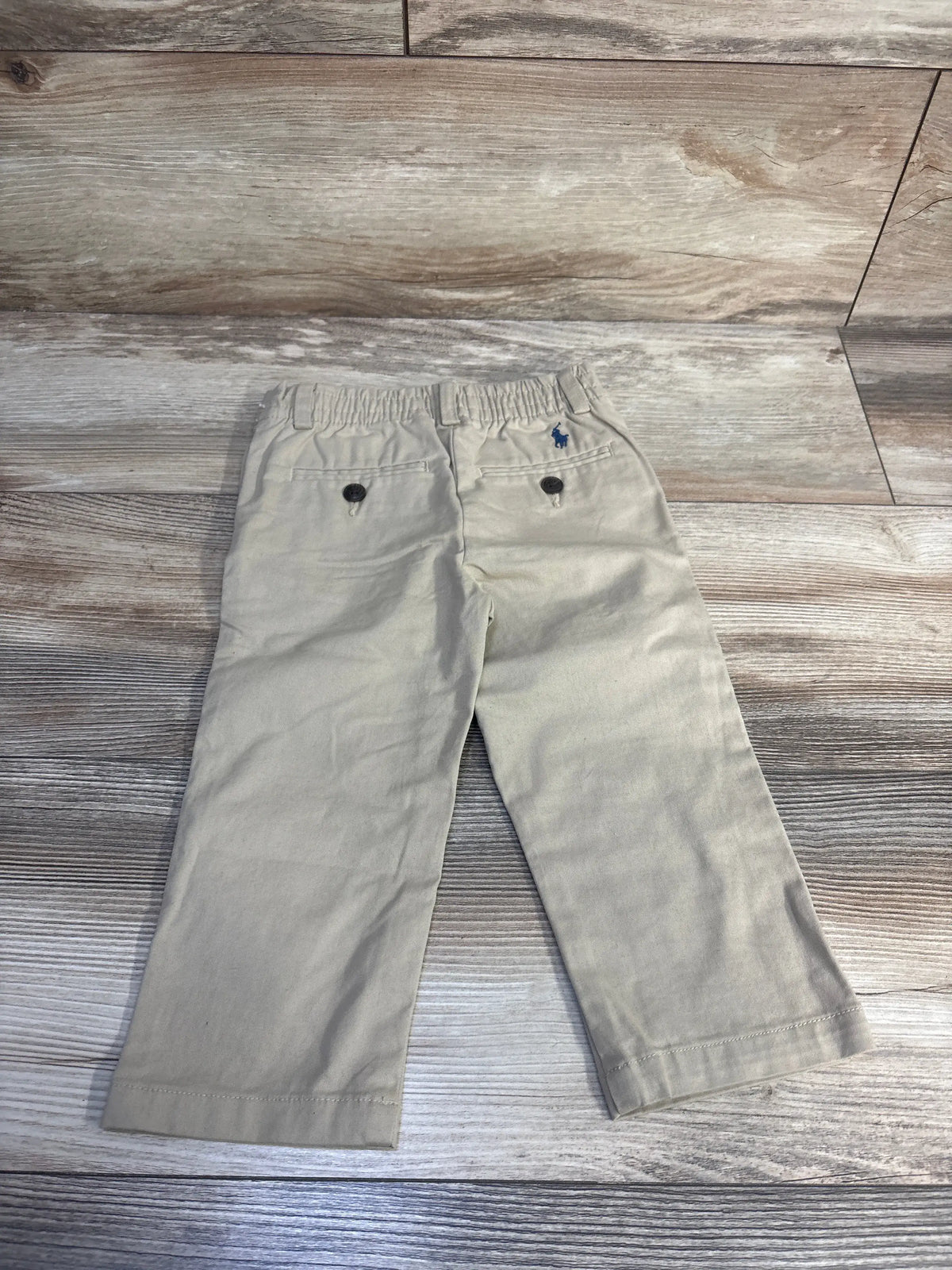 Back view of Ralph Lauren khaki stretch cotton chinos showcasing elasticized waist and button-welt back pockets on a wood-look background