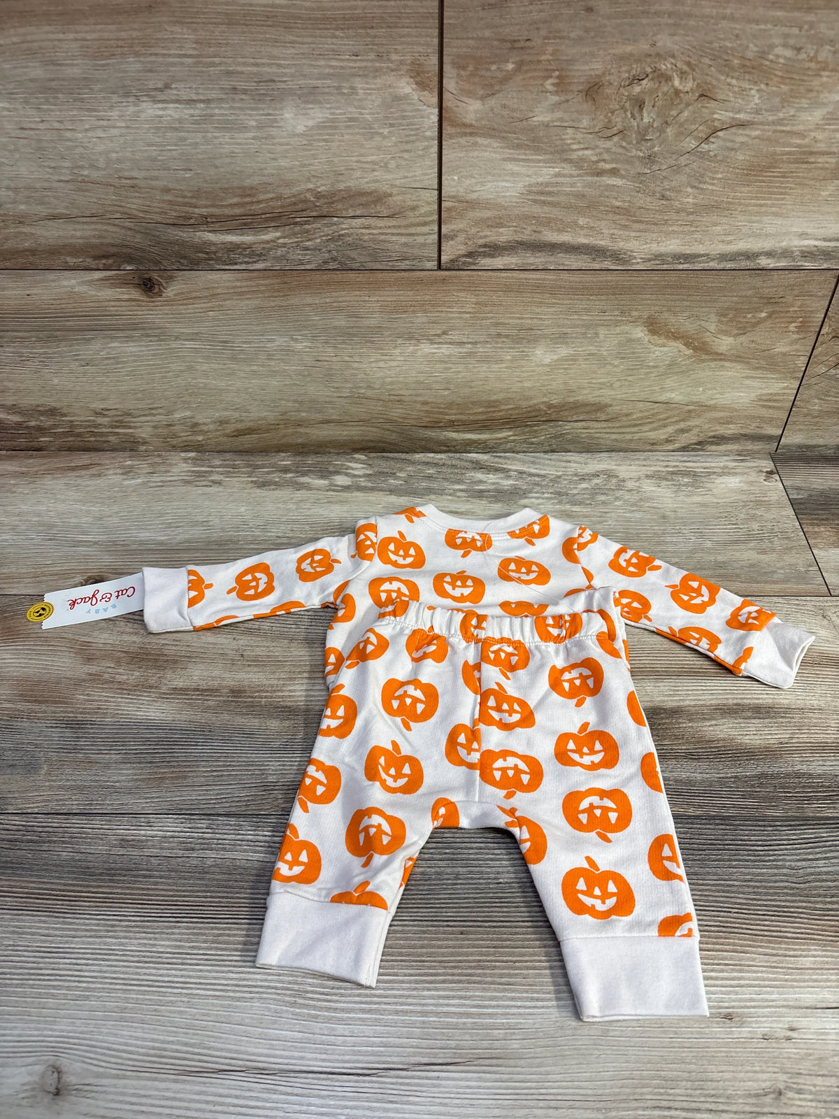 Flat lay of Cat & Jack newborn sweatshirt and jogger set showcasing orange jack o lantern print on white fabric with wood background