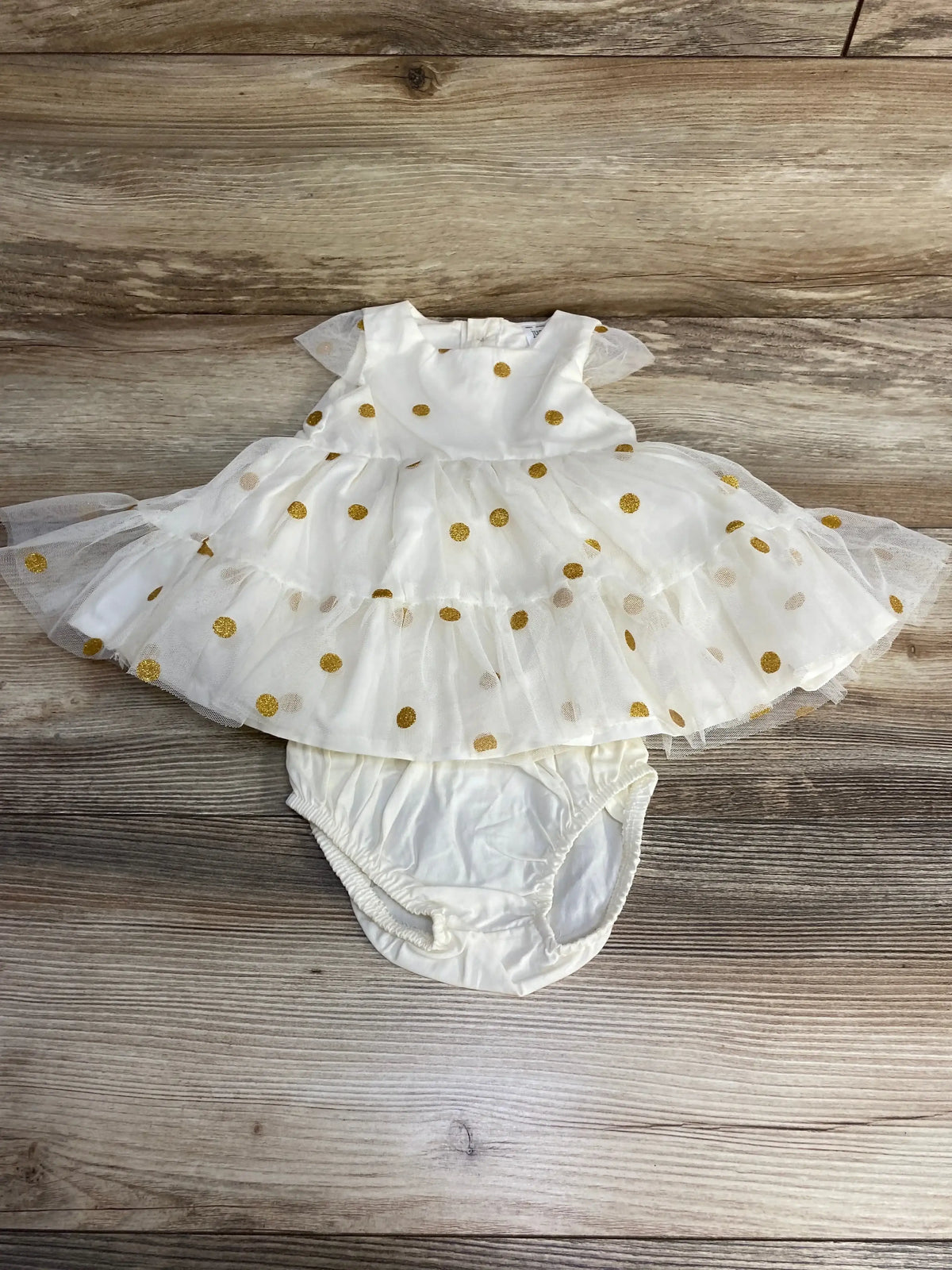 Flat lay of Just One You baby dress and bloomers showing tiered tulle skirt and gold glitter polka dots on wood background