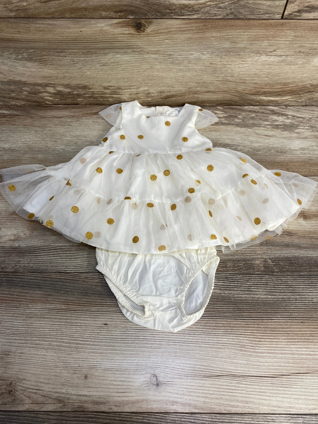 Flat lay of Just One You baby dress and bloomers showing tiered tulle skirt and gold glitter polka dots on wood background