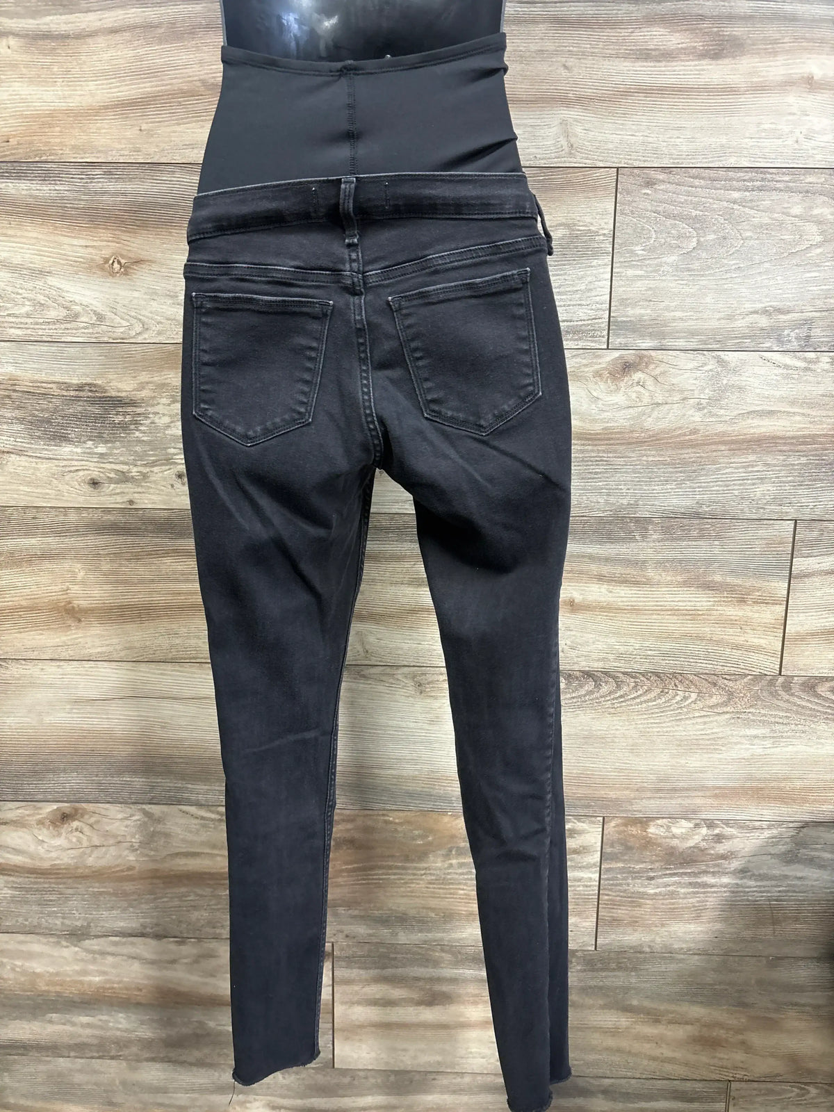 Back view of black maternity jeans leggings with full-panel waistband and skinny ankle legs on wood background, size S