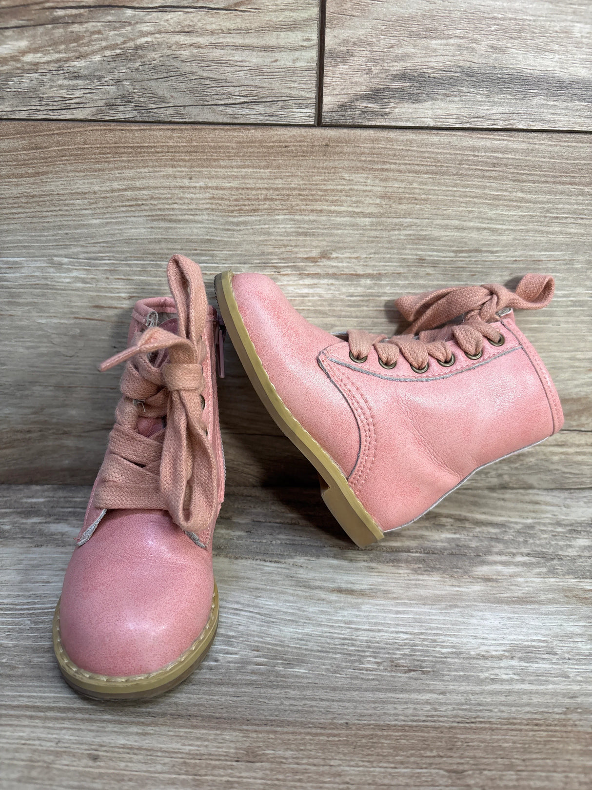 Pair of pink toddler lace-up boots with tan soles on wooden floor