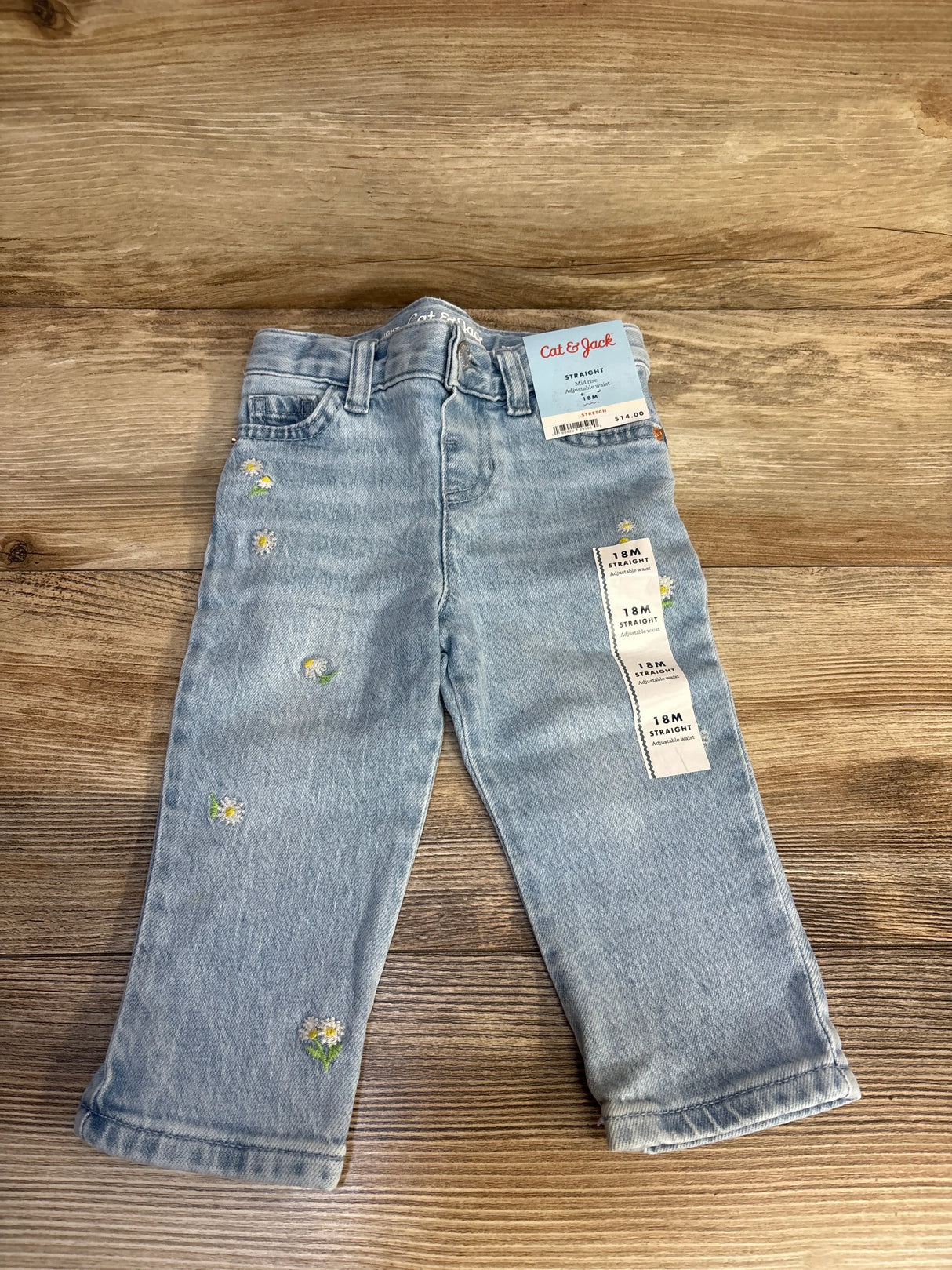 Light wash toddler jeans with daisy embroidery and straight leg style on wood background