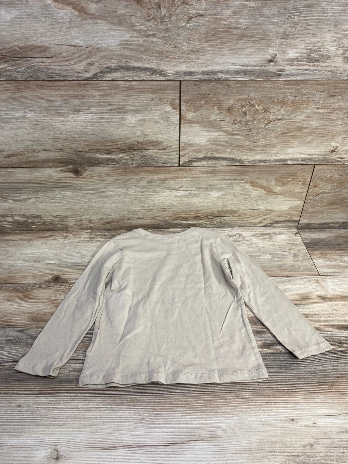 Beige long sleeve kids shirt laid flat on wood floor, back view, gently used clothing