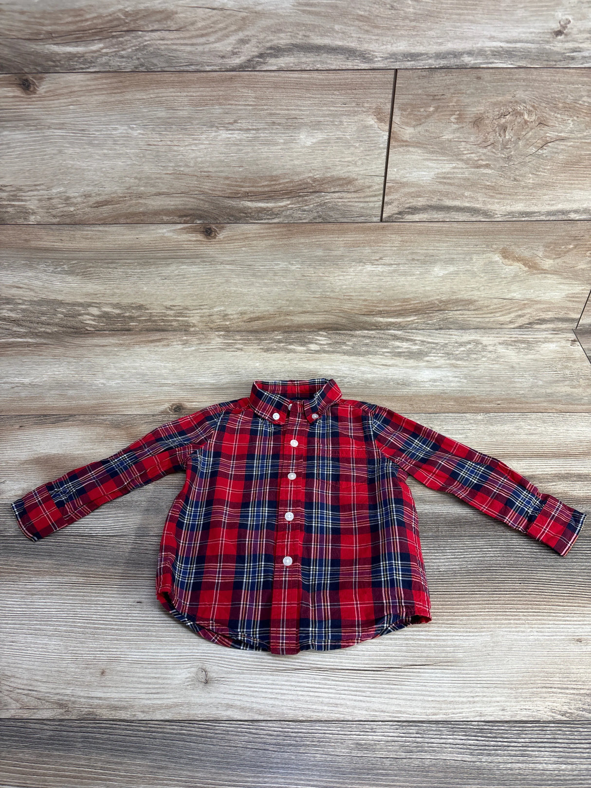 Red and navy blue plaid long-sleeve button-up kids shirt on wood floor background