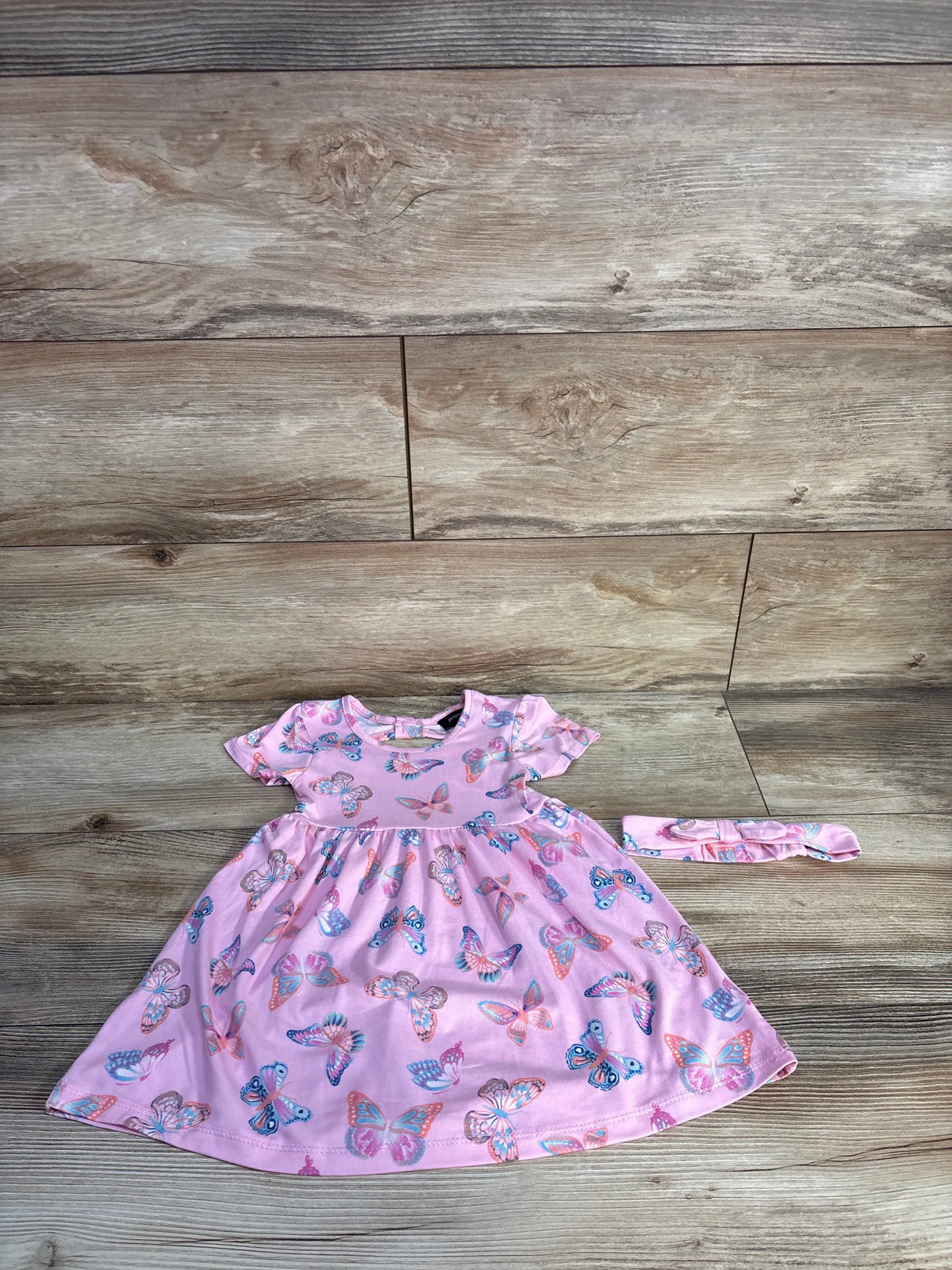 Front view of Picapino butterfly dress and matching headband set showcasing pink butterfly print on a wood look background
