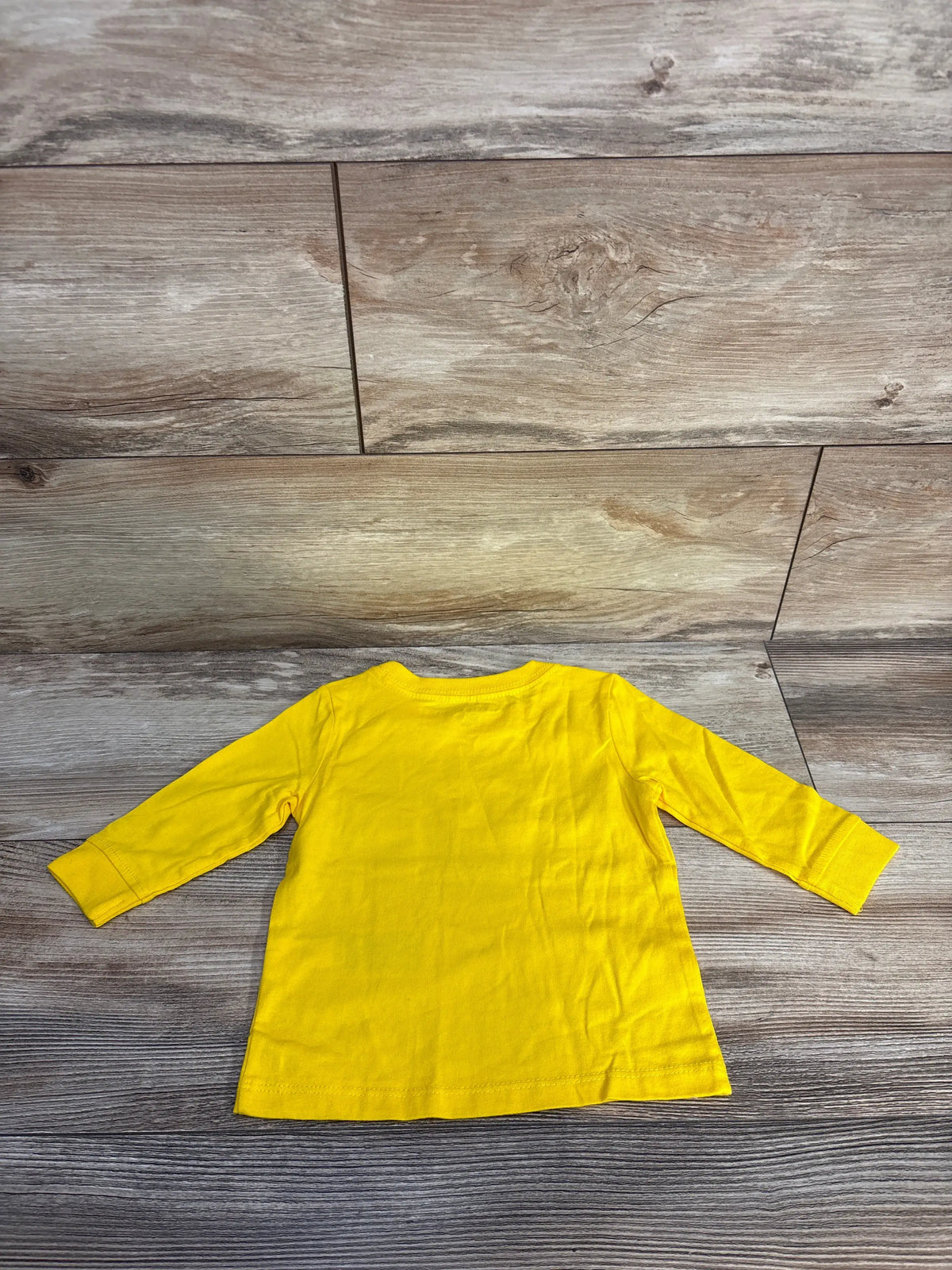 Back view of Tommy Hilfiger logo shirt showcasing bright yellow long sleeves on a wood-patterned floor