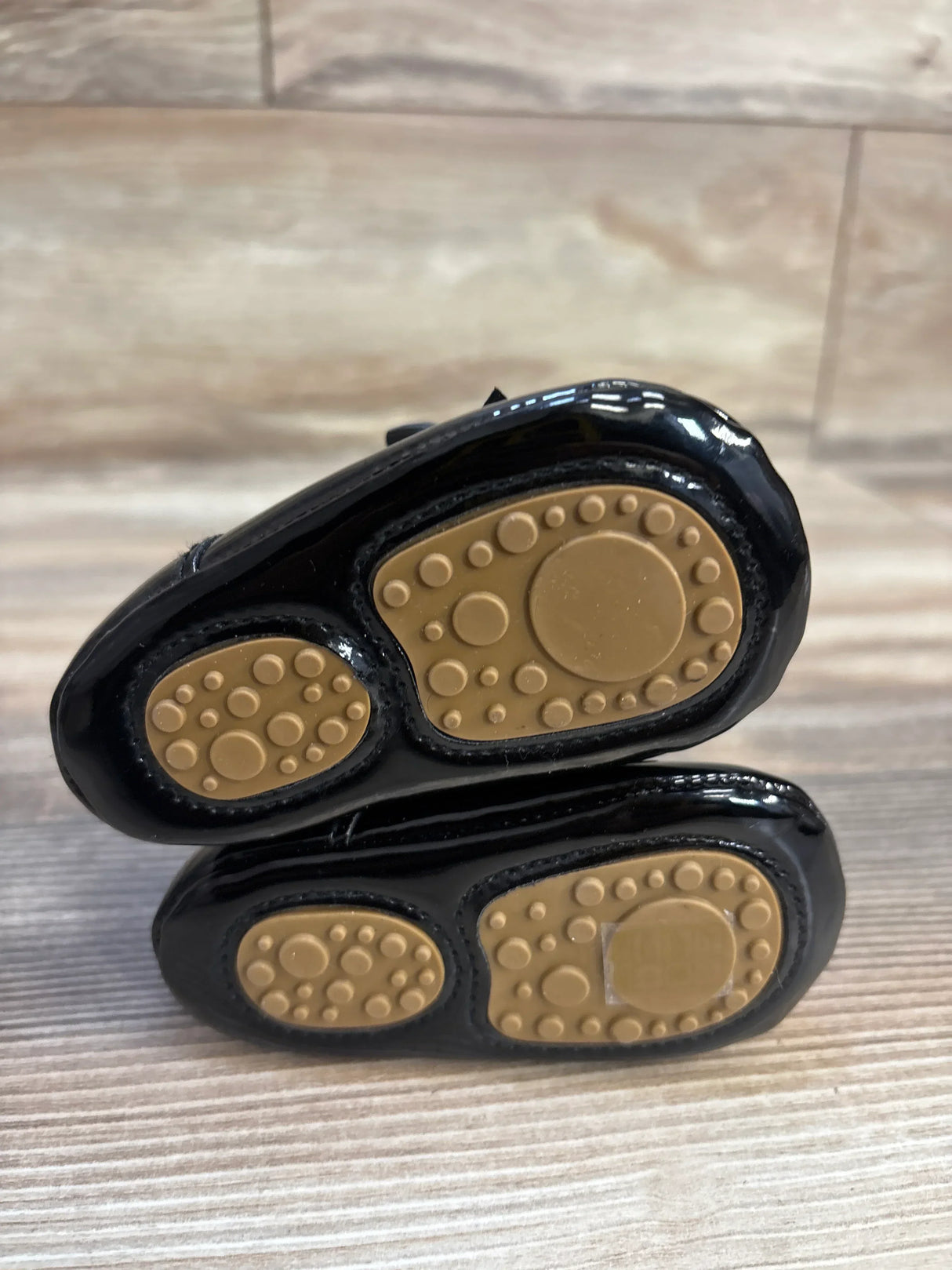 Black baby shoes with tan non-slip rubber soles on wood floor
