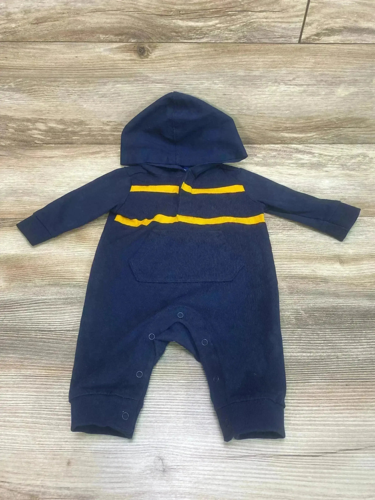 Front view of navy hooded baby coverall (0-3M) with yellow chest stripes, kangaroo pocket, and snap leg closures on wood
