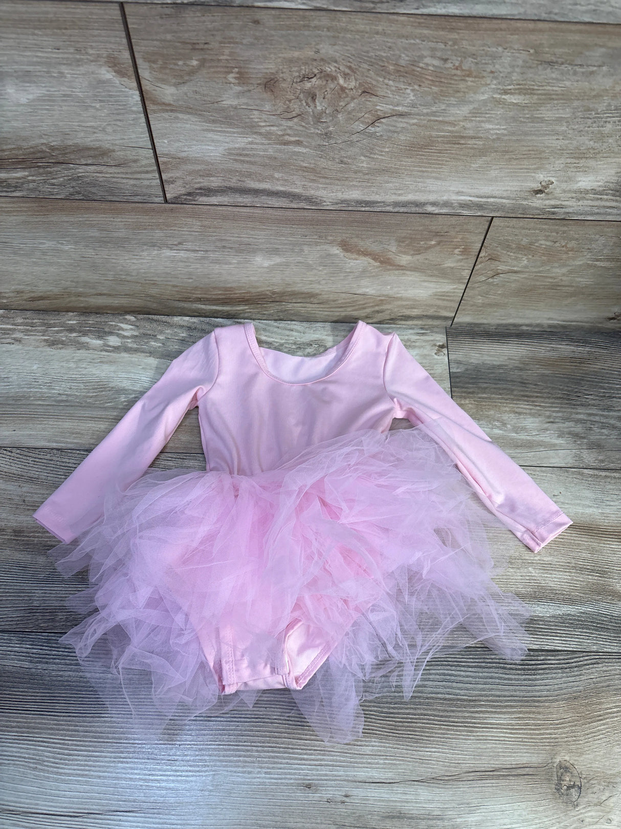 Flat lay of Kiijoy long sleeve pink tutu leotard showing layered tulle skirt and long sleeves on wood floor