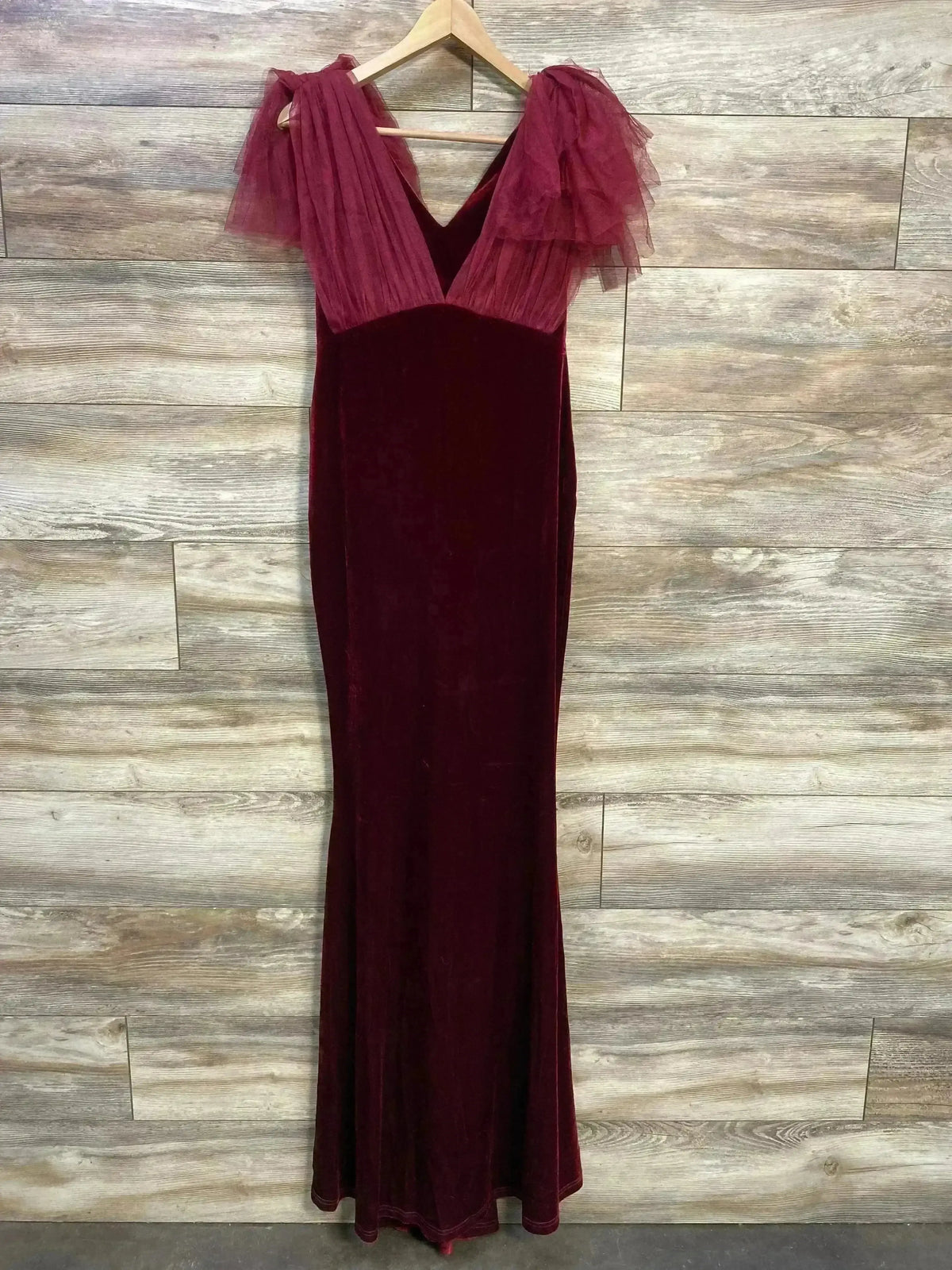 Front view of burgundy velvet maternity mermaid dress showcasing V-neck and contrast mesh puff sleeves with wood-plank background