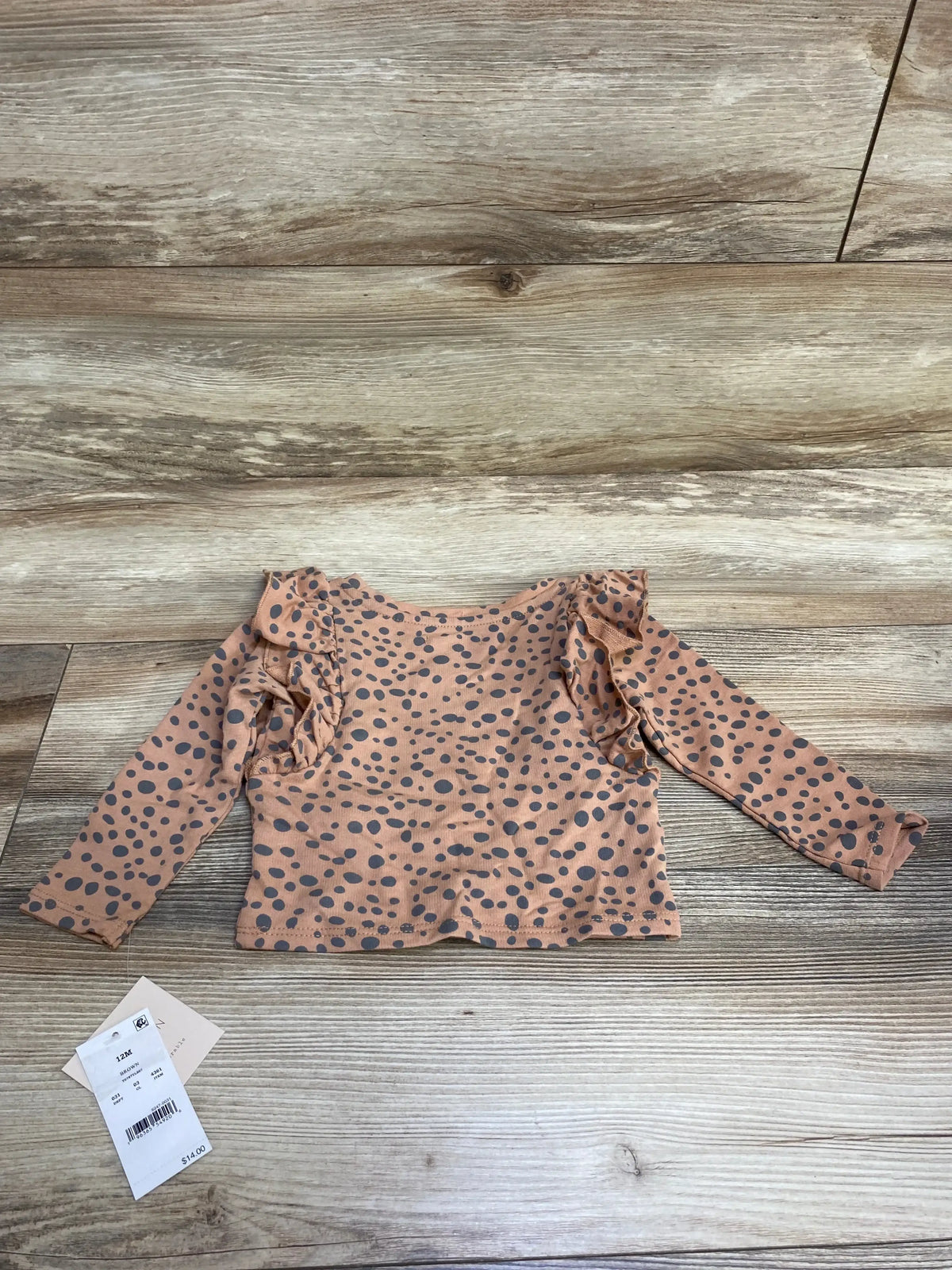 Top view of brown NEW Grayson Mini Ruffled Polka Dot Top, size 12M, with long sleeves and shoulder ruffles on wood background