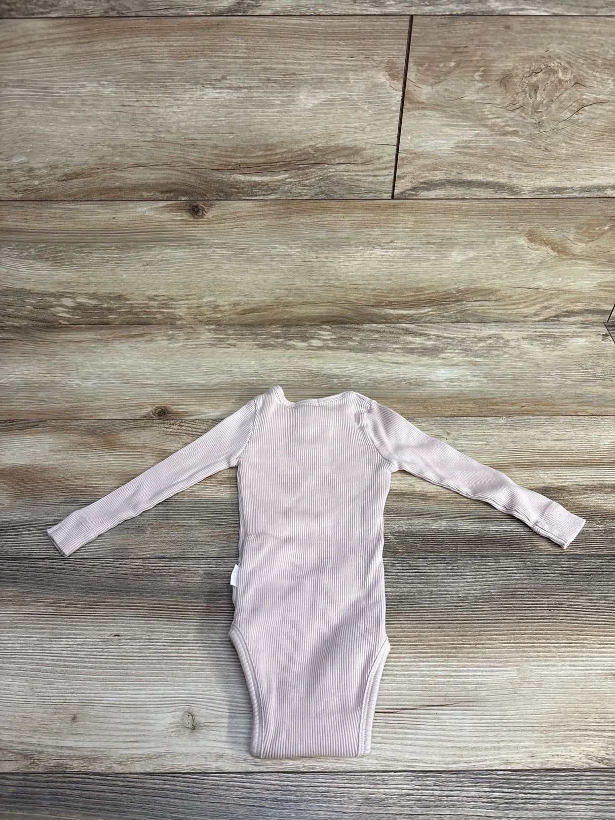 Light pink ribbed long-sleeve baby bodysuit laid flat on rustic wooden floor