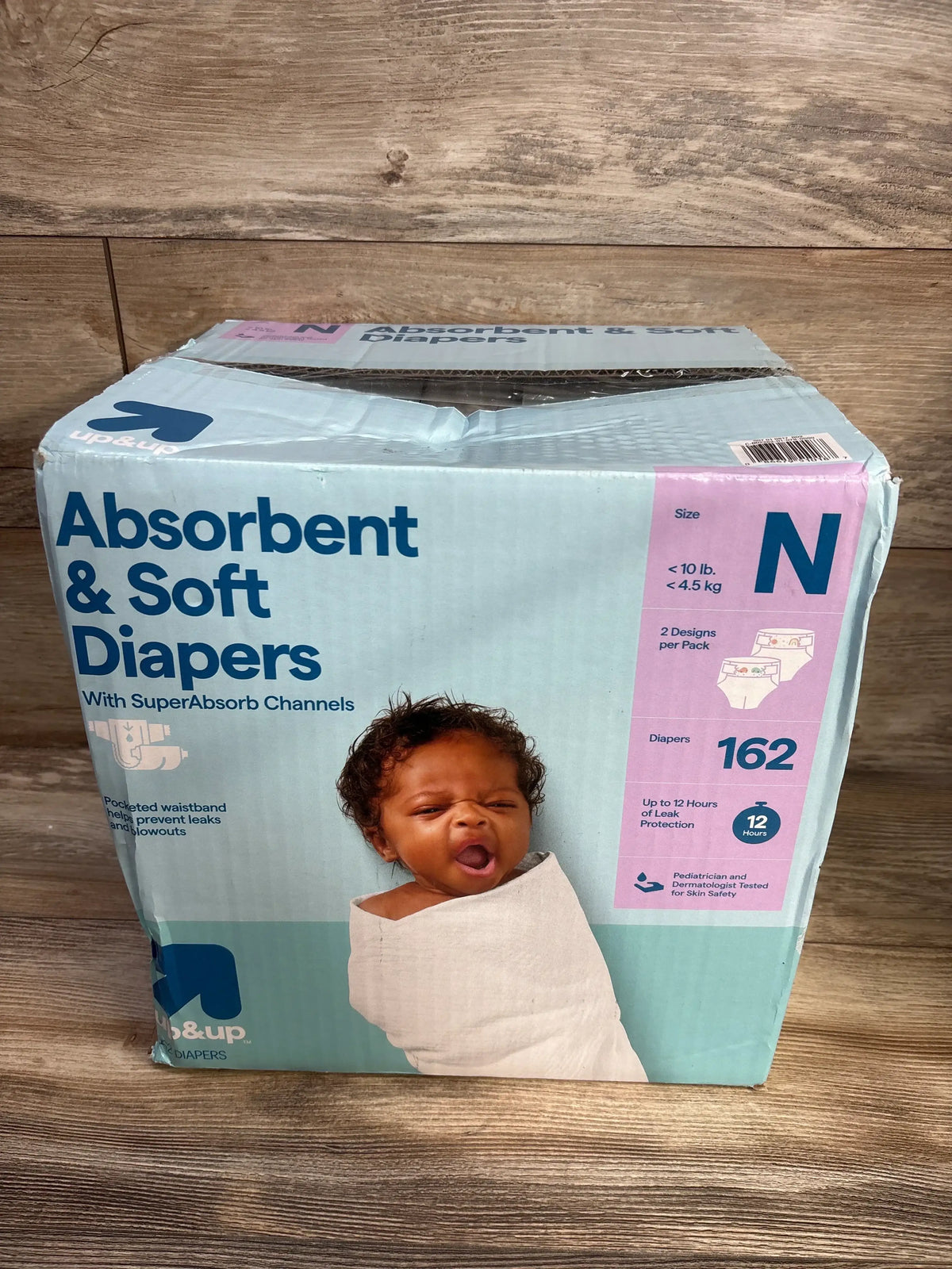 Front view of up&up newborn diaper box showing ‘Absorbent & Soft Diapers’, ‘162 diapers’, and baby image on a wood floor background
