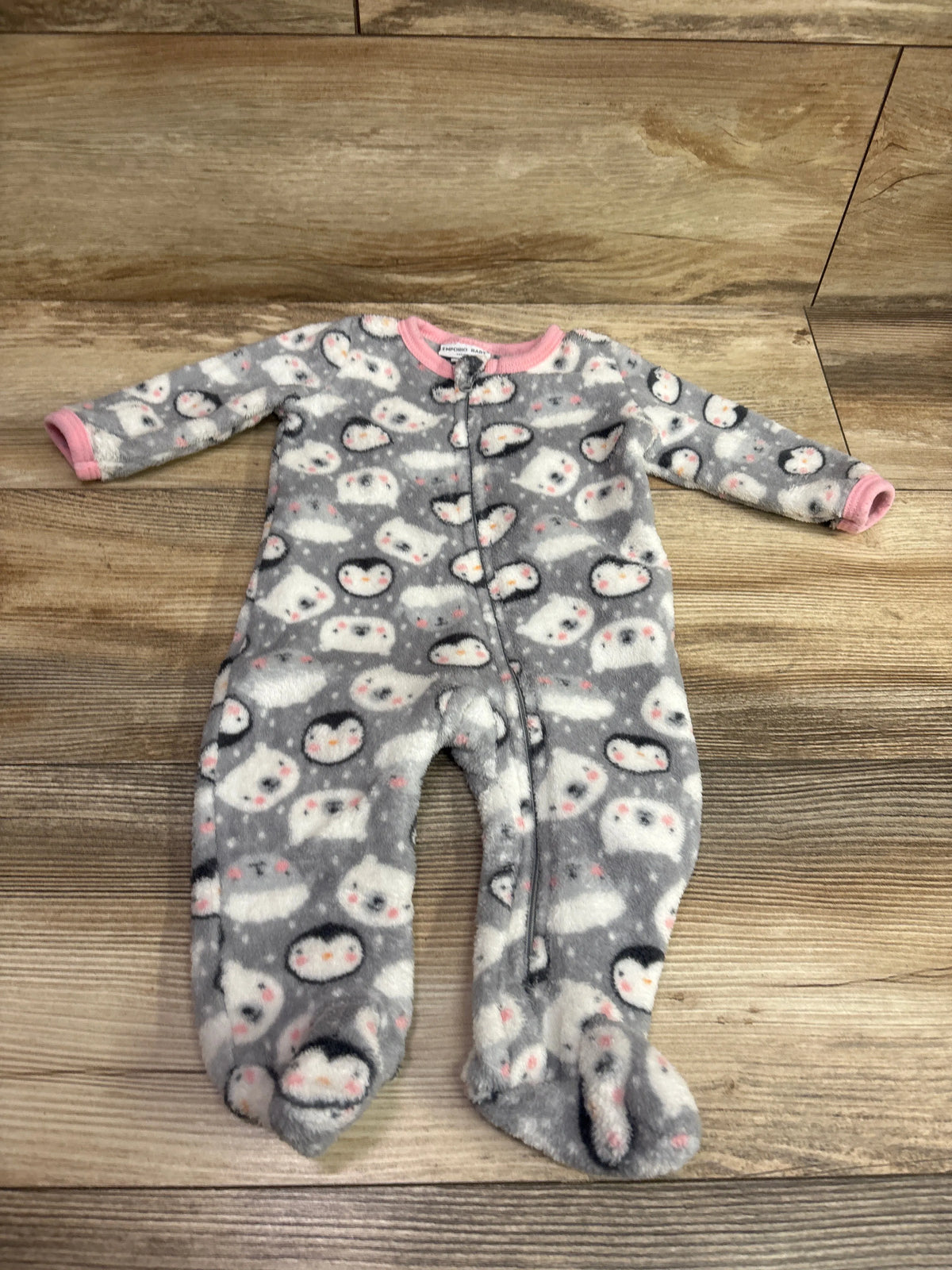 Front view of Emporio baby blanket sleeper, grey with penguin print, pink trim, zipper, and footed legs on wood floor