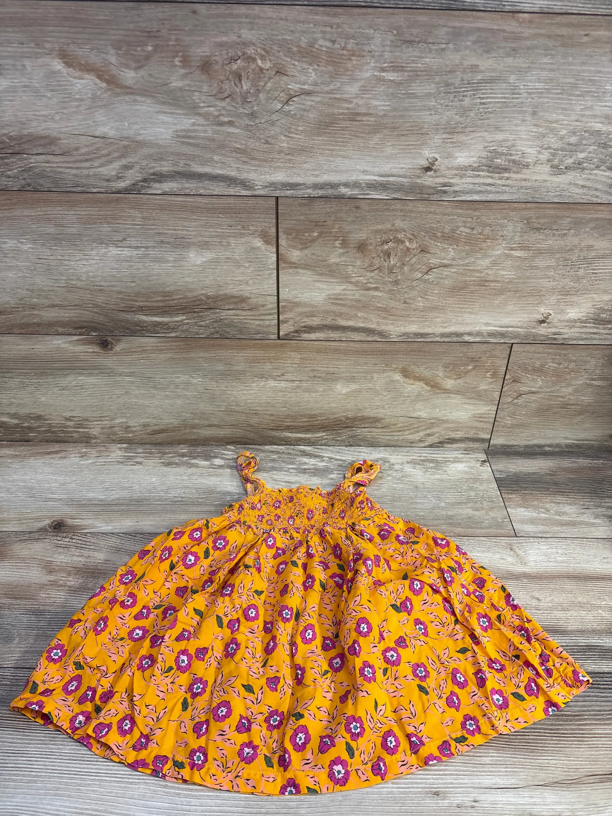 Flat lay of Carter’s orange floral smocked dress, size 24m, showing smocked bodice and ruffle straps on wood background