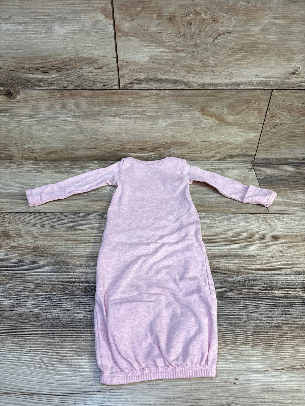 Light pink long sleeve baby gown with elastic hem on wood background