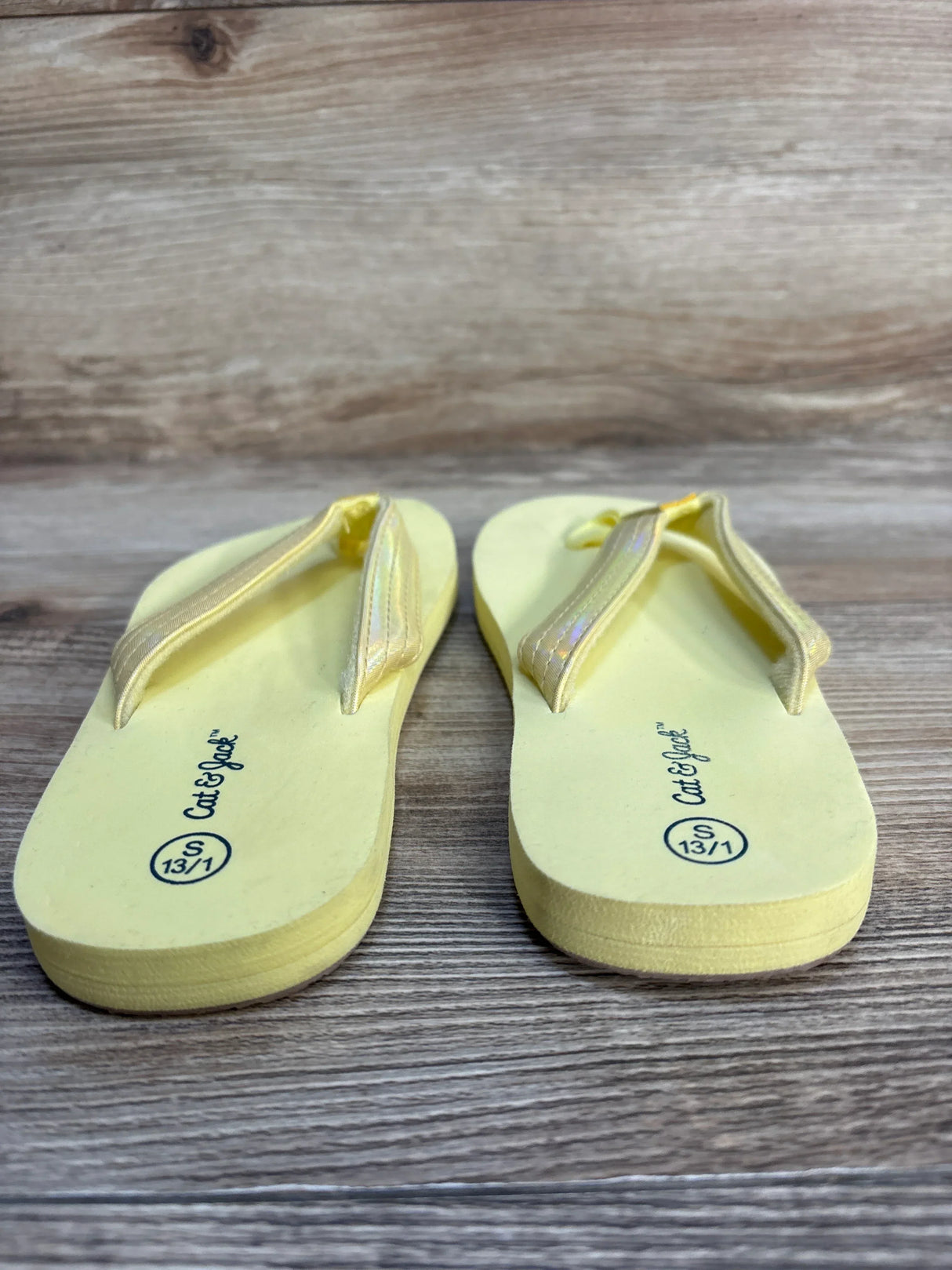 Yellow kids flip flops with glitter straps, size 13/1, on wood background