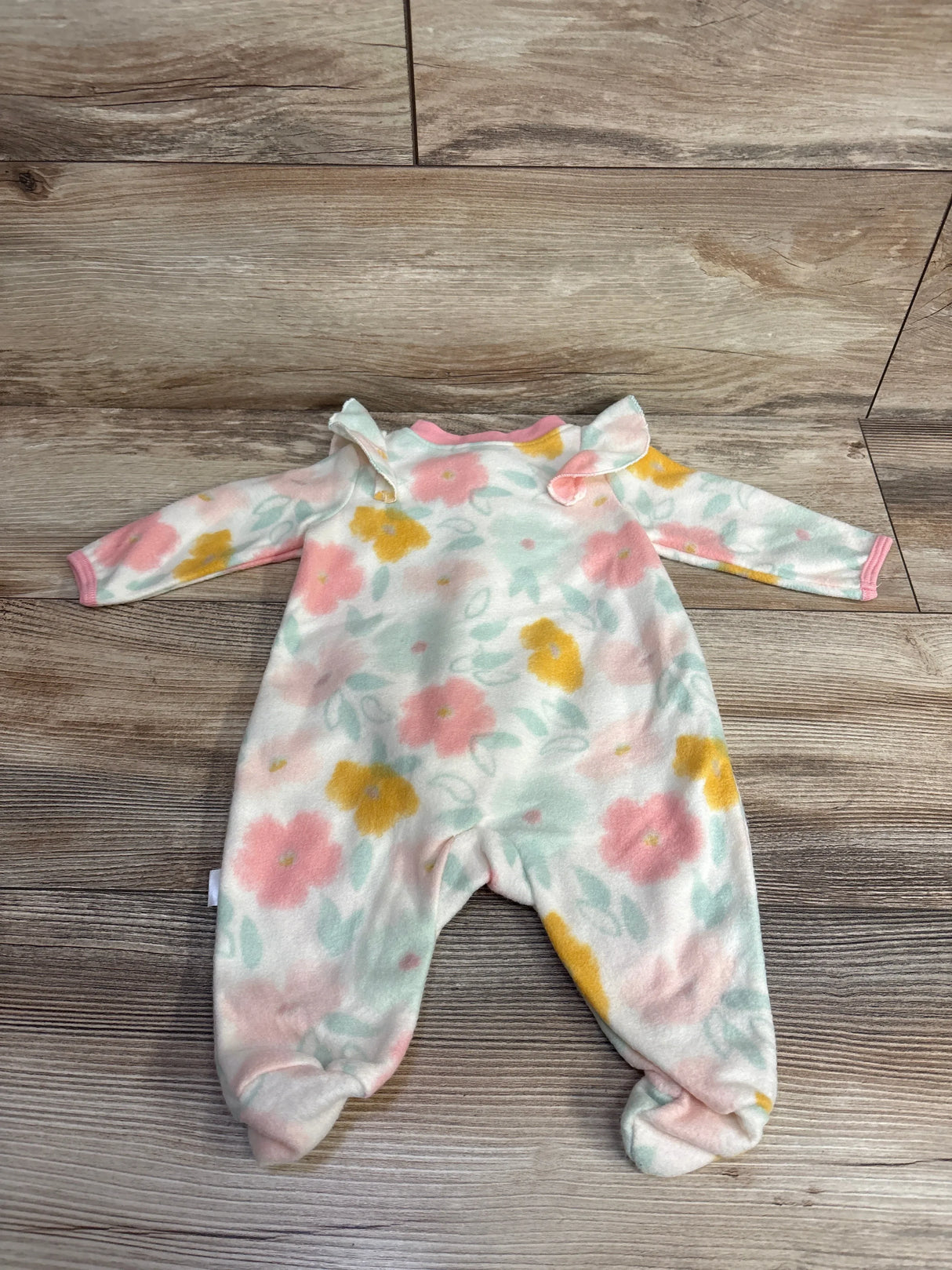 Baby fleece footed sleeper with pink, yellow, and green floral pattern on wood floor