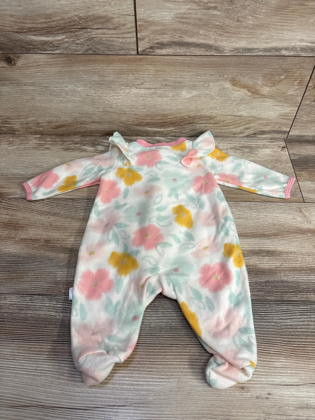 Baby fleece footed sleeper with pink, yellow, and green floral pattern on wood floor