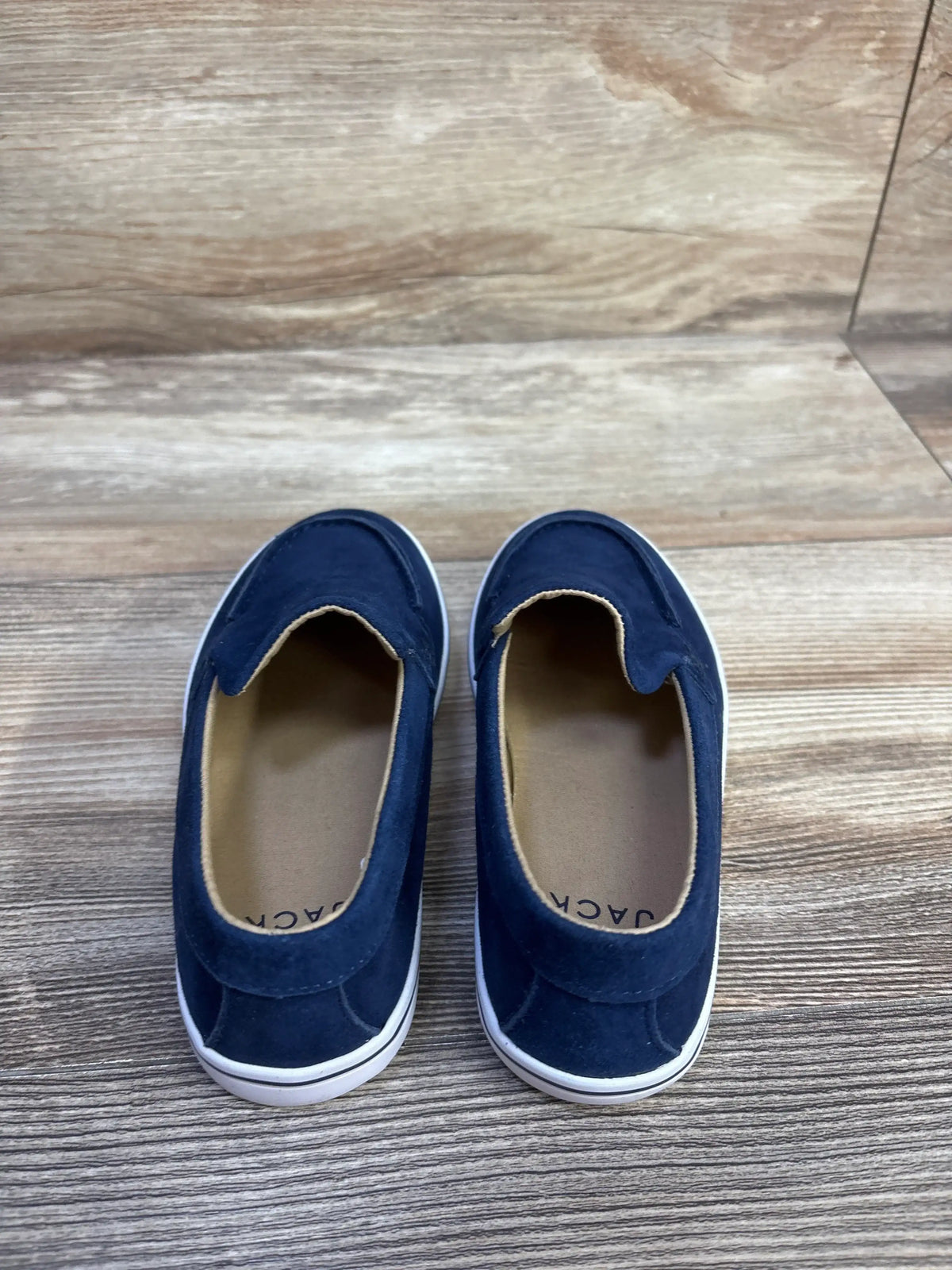 Top view of Janie & Jack blue suede slip-on sneakers showcasing white soles on a wood-look floor