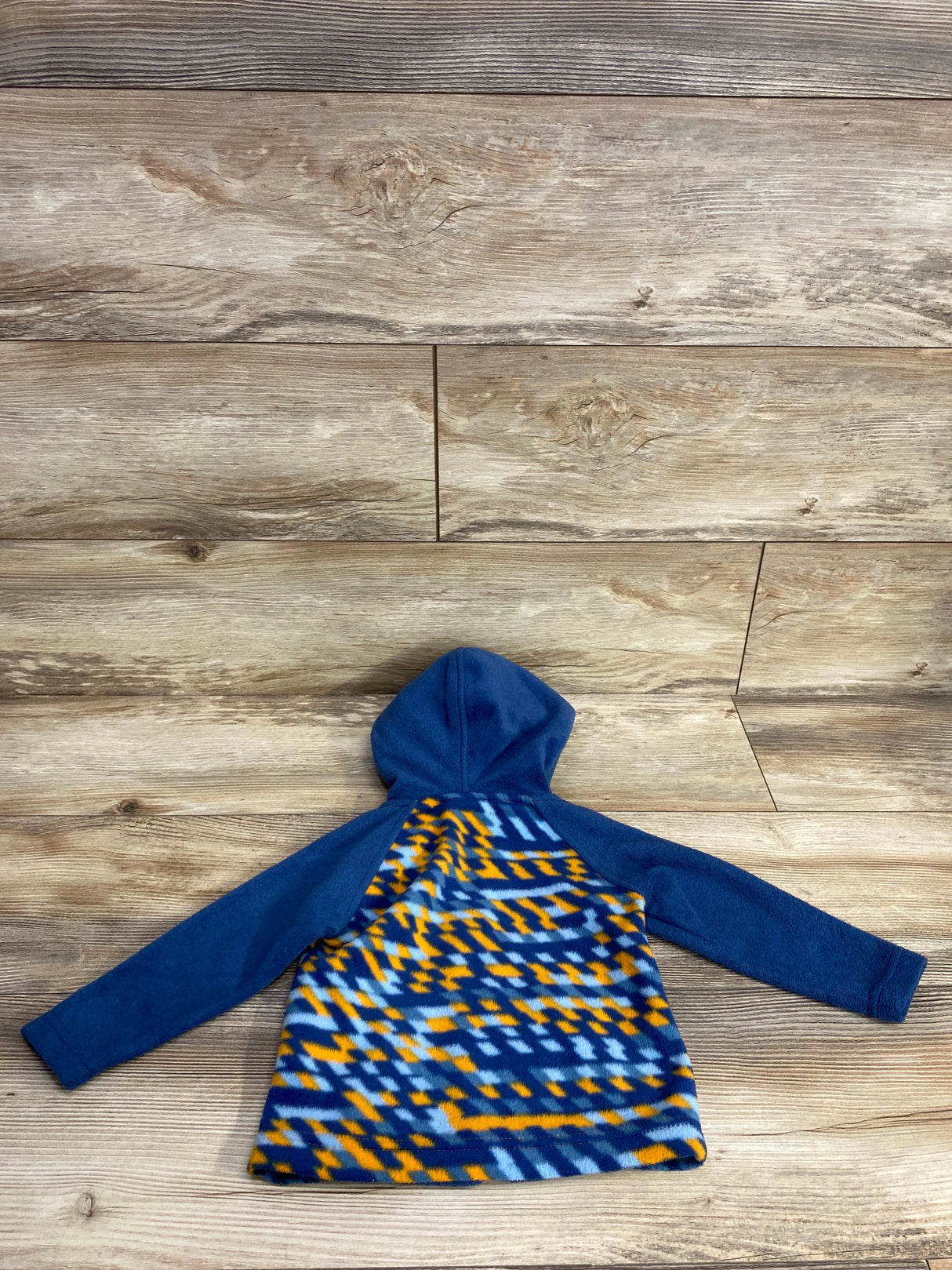 Blue hooded fleece jacket with orange and light blue geometric pattern on wooden floor