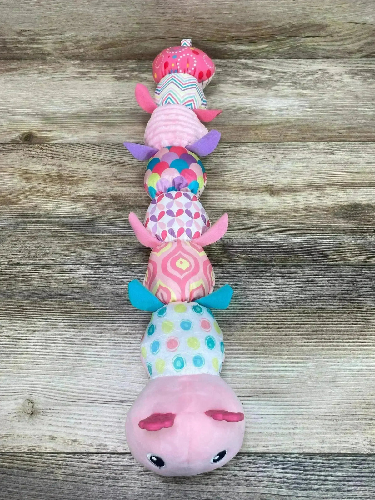 Top-down view of pink musical caterpillar toy showcasing patterned segments and sensory crinkle and rattle on wood background