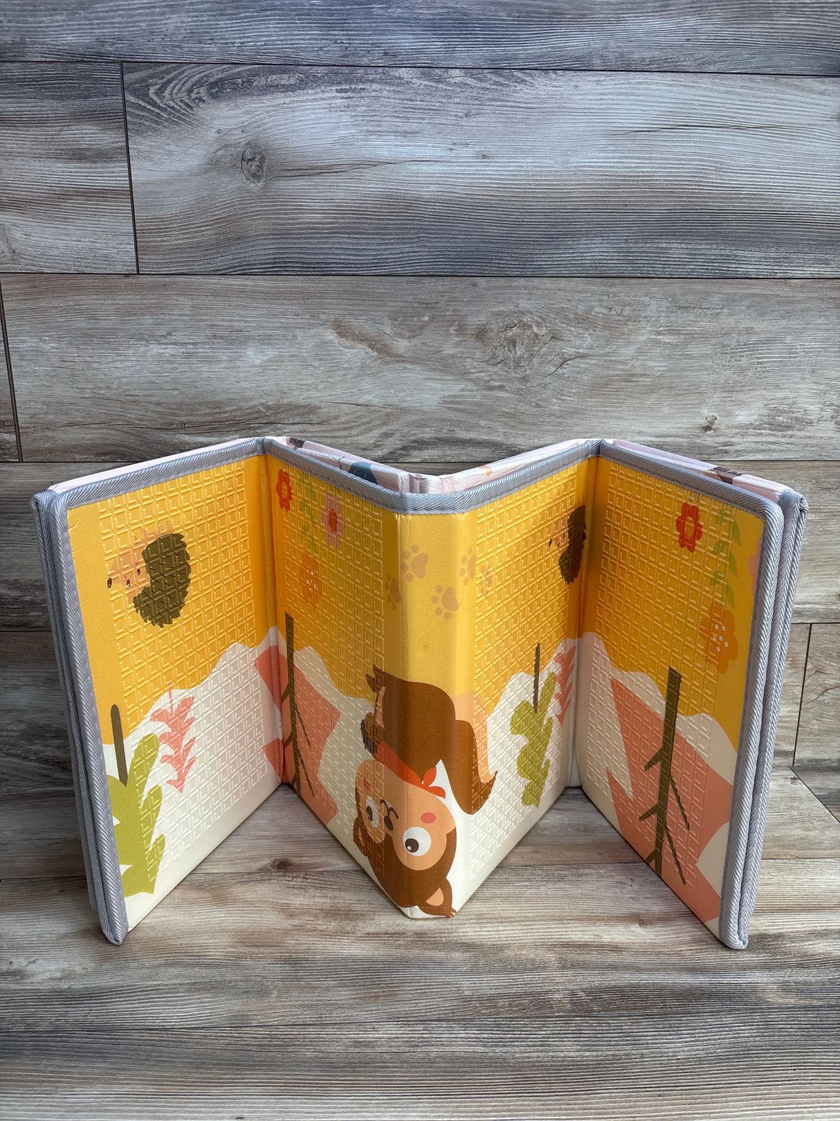 Foldable baby play mat with cartoon bear and hedgehog, wood floor background