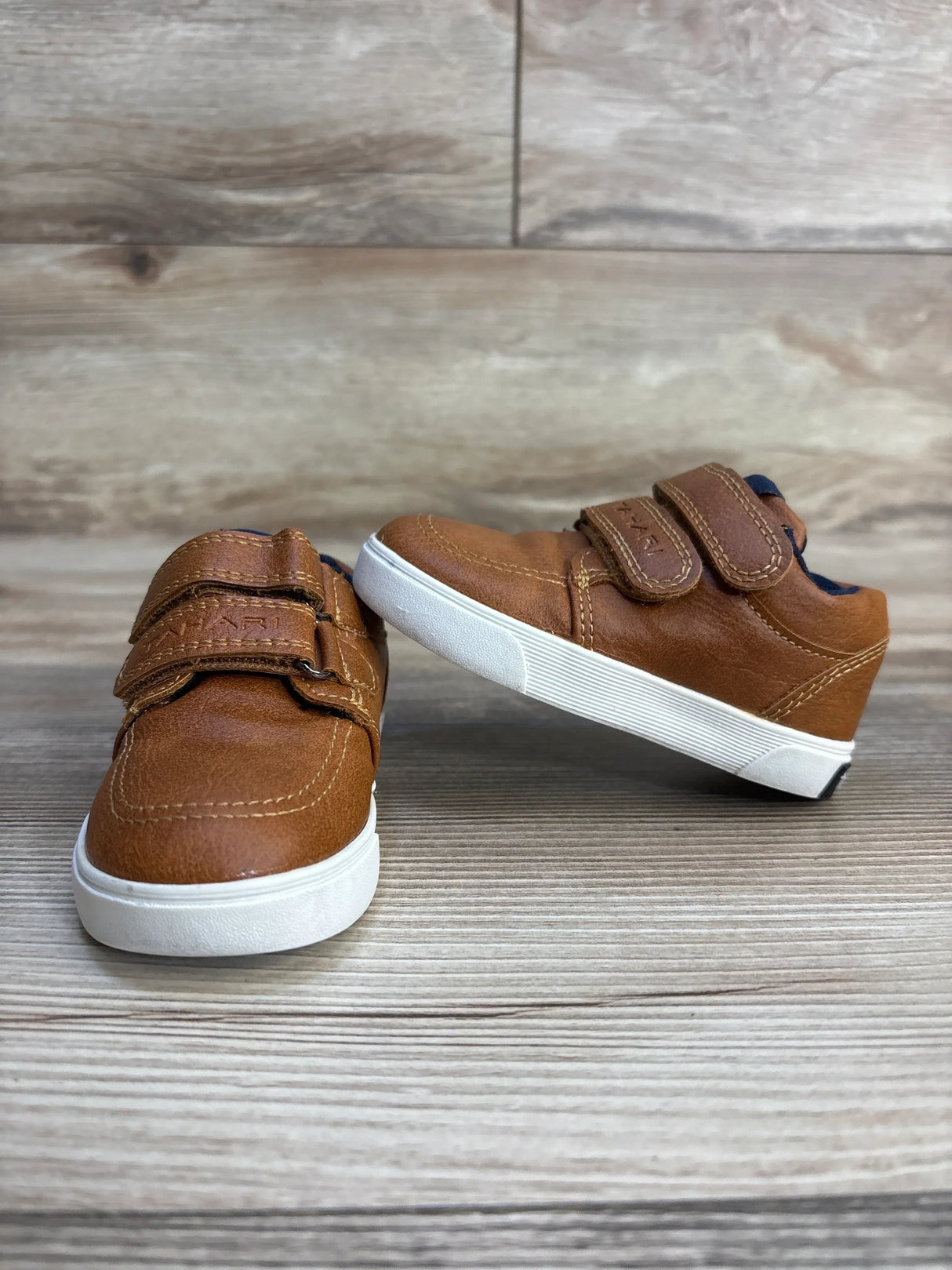 Front three-quarter view of Tahari Double Strap toddler sneakers in brown showing double Velcro straps and white rubber soles on light wood floor