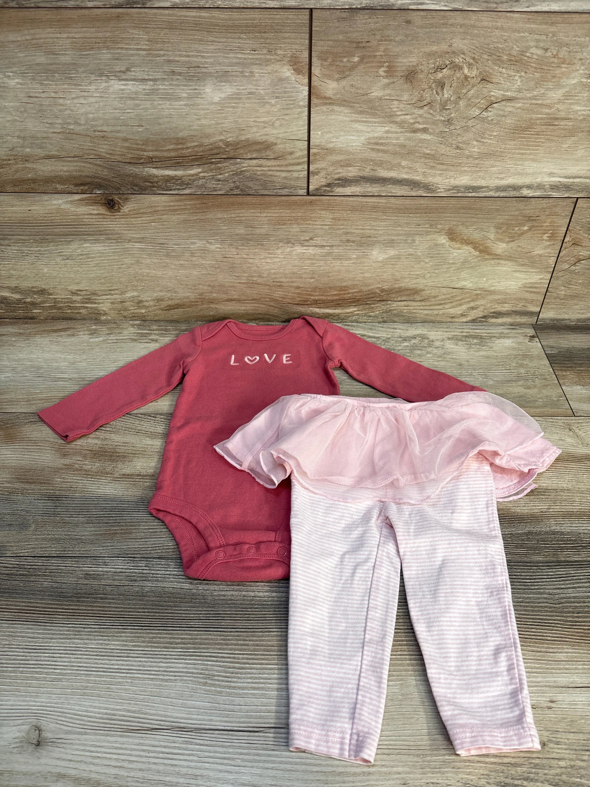 Pink baby girl outfit with 'LOVE' bodysuit and striped tutu leggings on wood floor