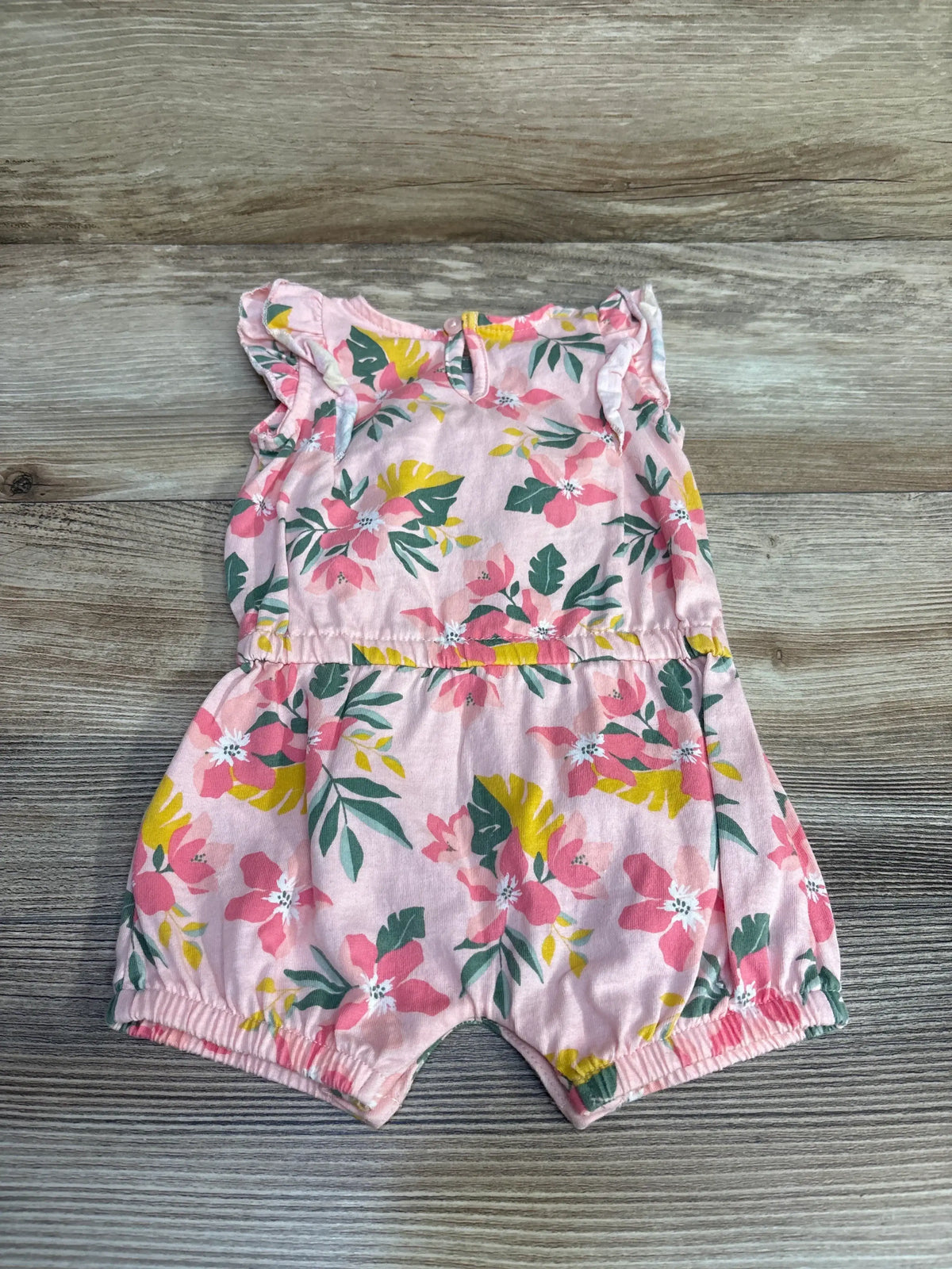 Flat lay of pink floral ruffle romper size 3M showcasing ruffle sleeves, elastic leg openings, and gathered waist on wood background