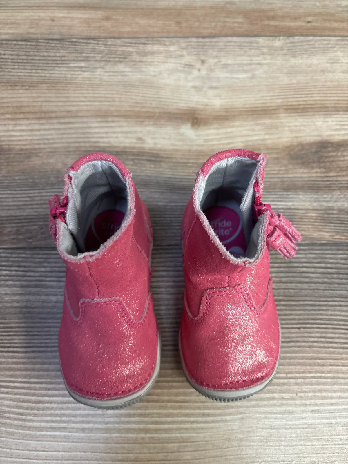 Top view of Stride Rite SRT Zoe pink ankle boots showing glittery suede finish and side zipper with tassel on wood floor