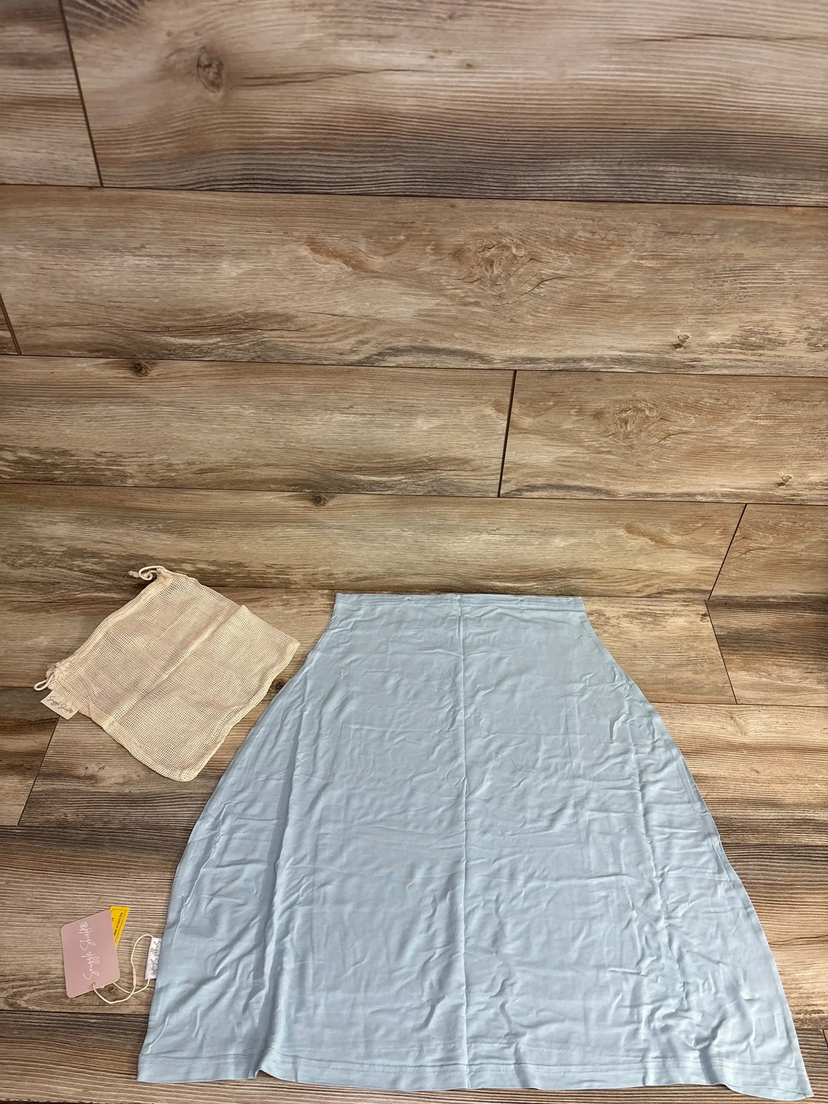 Top-down view of Snuggle Sheild LUXE nursing and car seat cover in light blue showing front snap and mesh bag on wood floor
