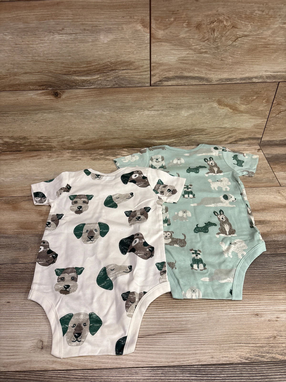 Two Member's Mark baby bodysuits with green dog prints on white and sage green fabric.