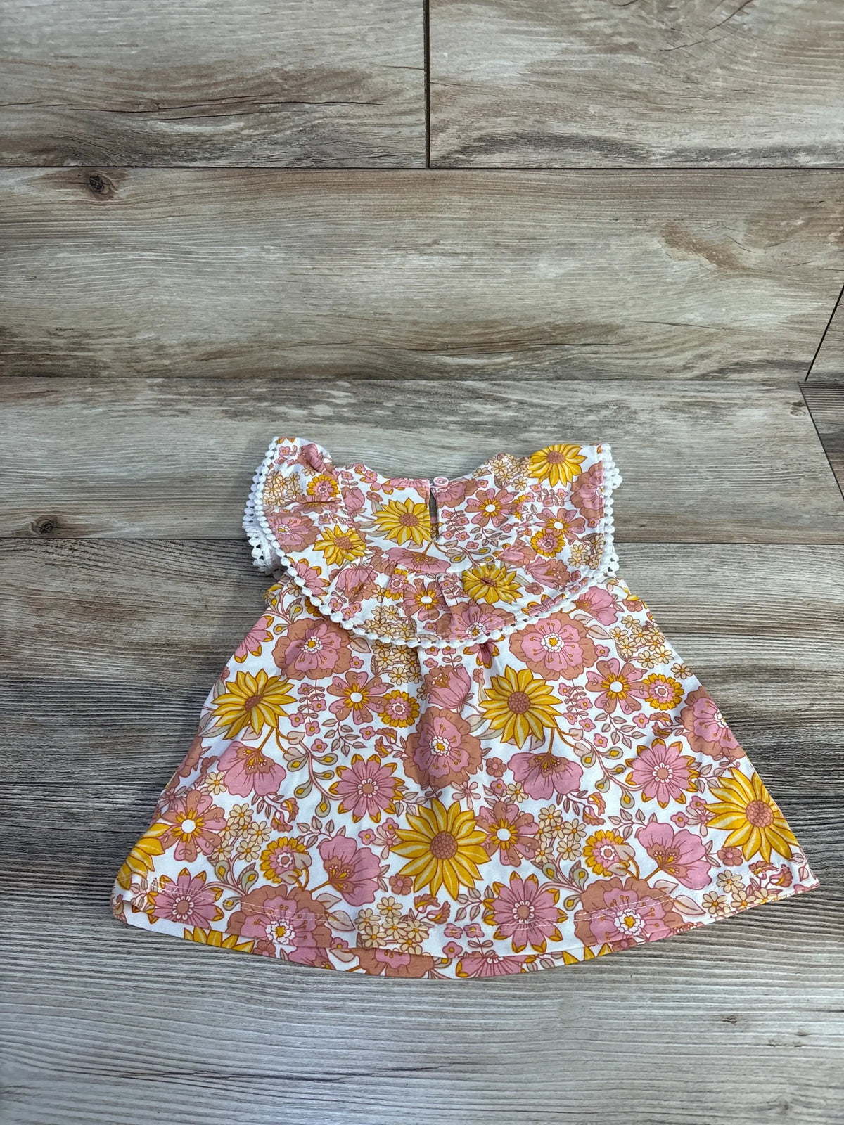 Flat lay of C&C California baby dress with pink and yellow floral print and lace-trimmed ruffle collar on wood background