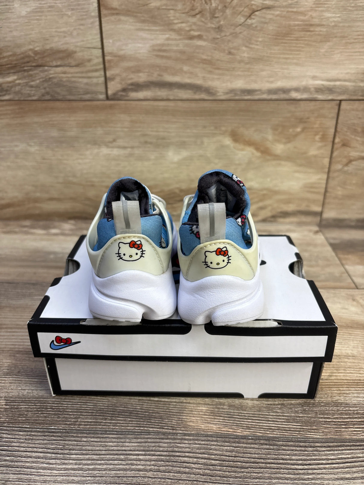 Rear view of Hello Kitty x Nike Air Presto TD toddler sneakers showcasing Hello Kitty heel graphic with Nike box on wood floor