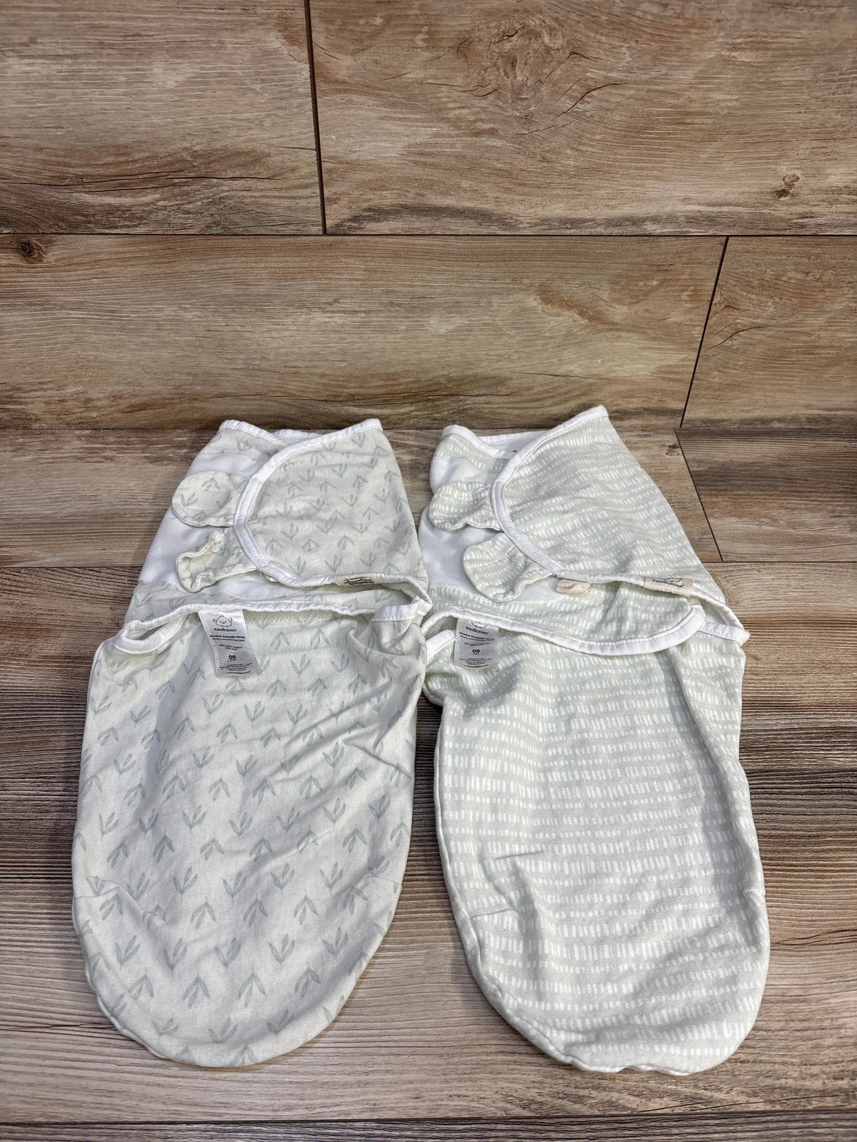Front view of KeaBabies Soothe Swaddle Wrap 2pk showcasing two green wraps with leaf and stripe patterns on wood floor