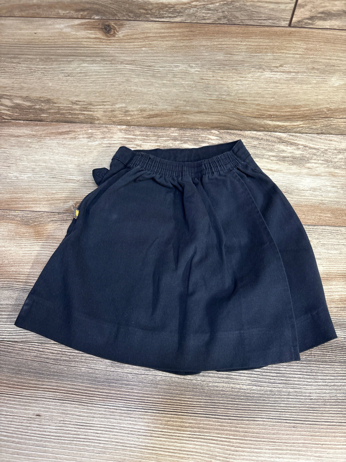 Black elastic waist skirt on wooden floor, kids clothing flat lay