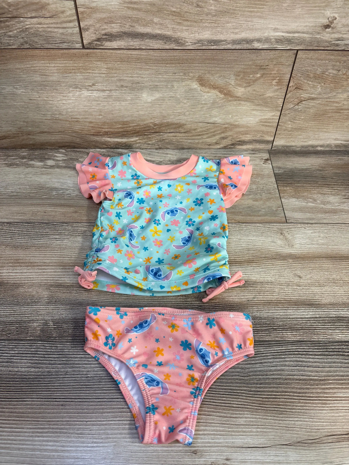 Flat lay of Disney Stitch two-piece rash guard and bikini bottoms showcasing blue floral print and pink ruffles
