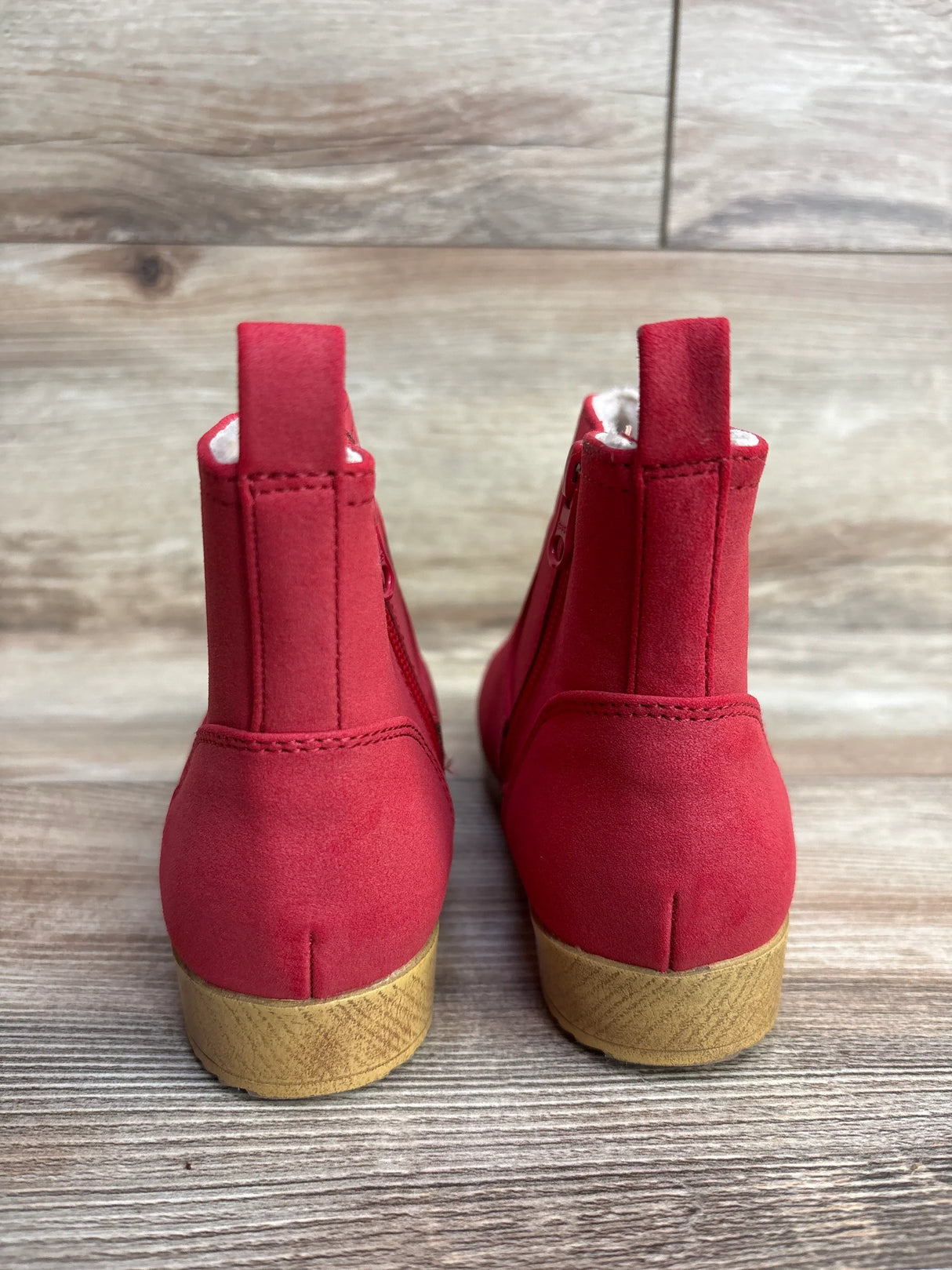 Back view of red suede children’s ankle boots with tan rubber soles on wooden floor