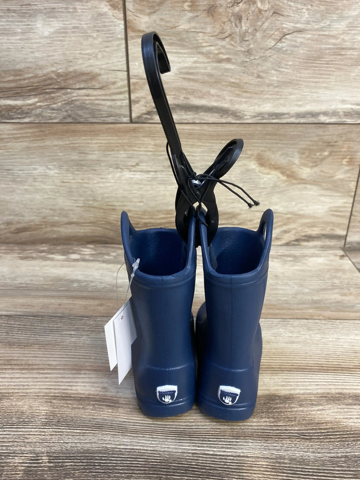 Rear view of navy BEARPAW EVA toddler rain boots showing pull-on handles and heel logo on wood-look floor
