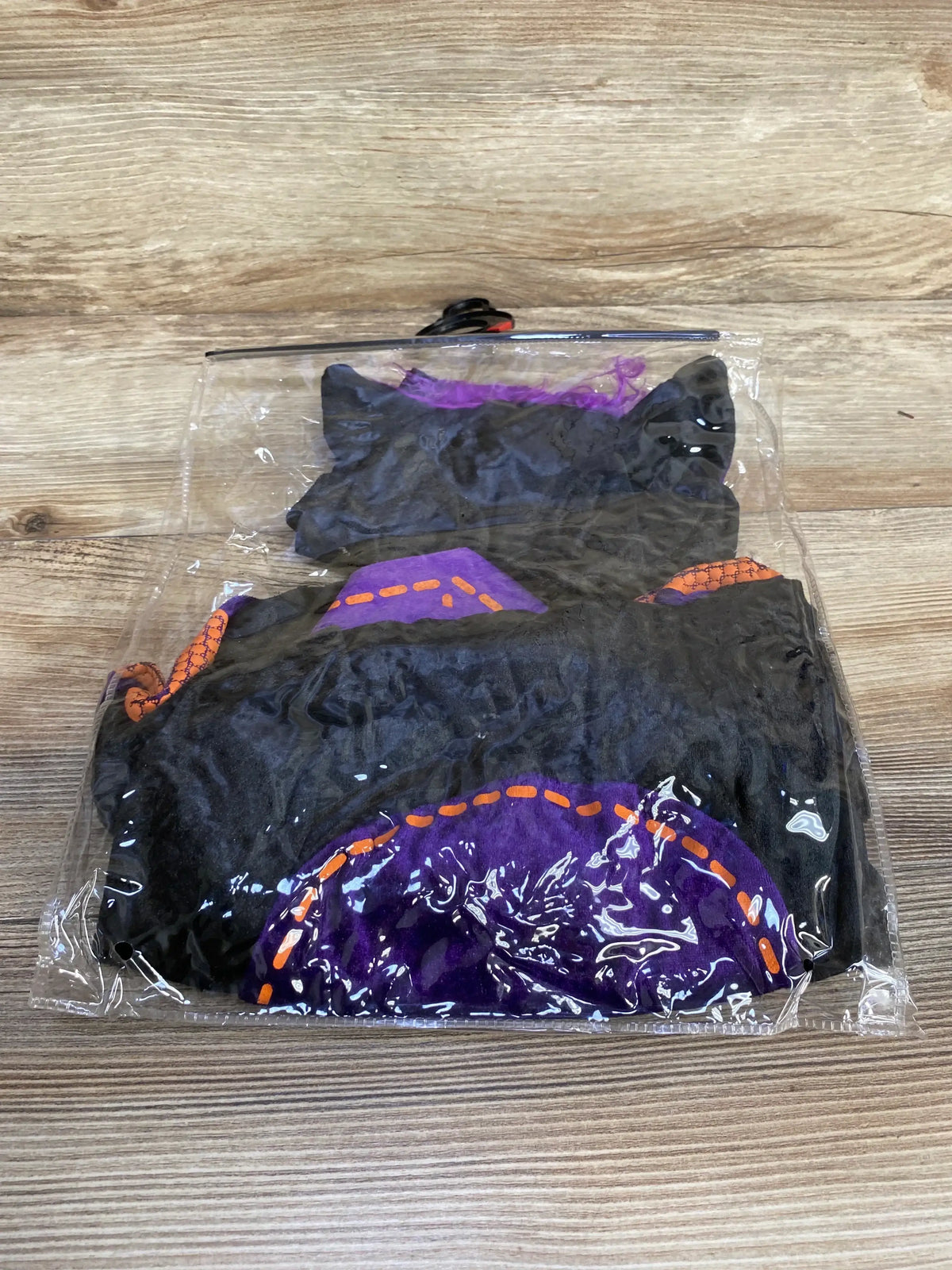 Front view of black InCharacter baby bat costume with bat ears and purple and orange accents in clear packaging