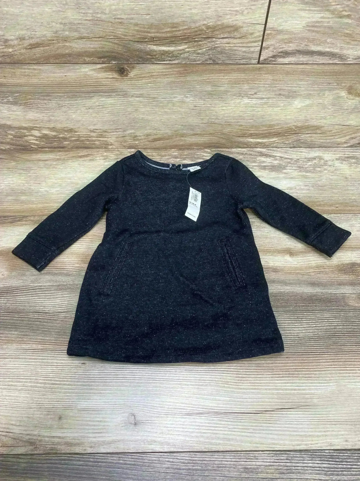 Flat lay of Old Navy fleece shift dress in black, toddler size 12-18M with long sleeves and front pockets on wood-look floor