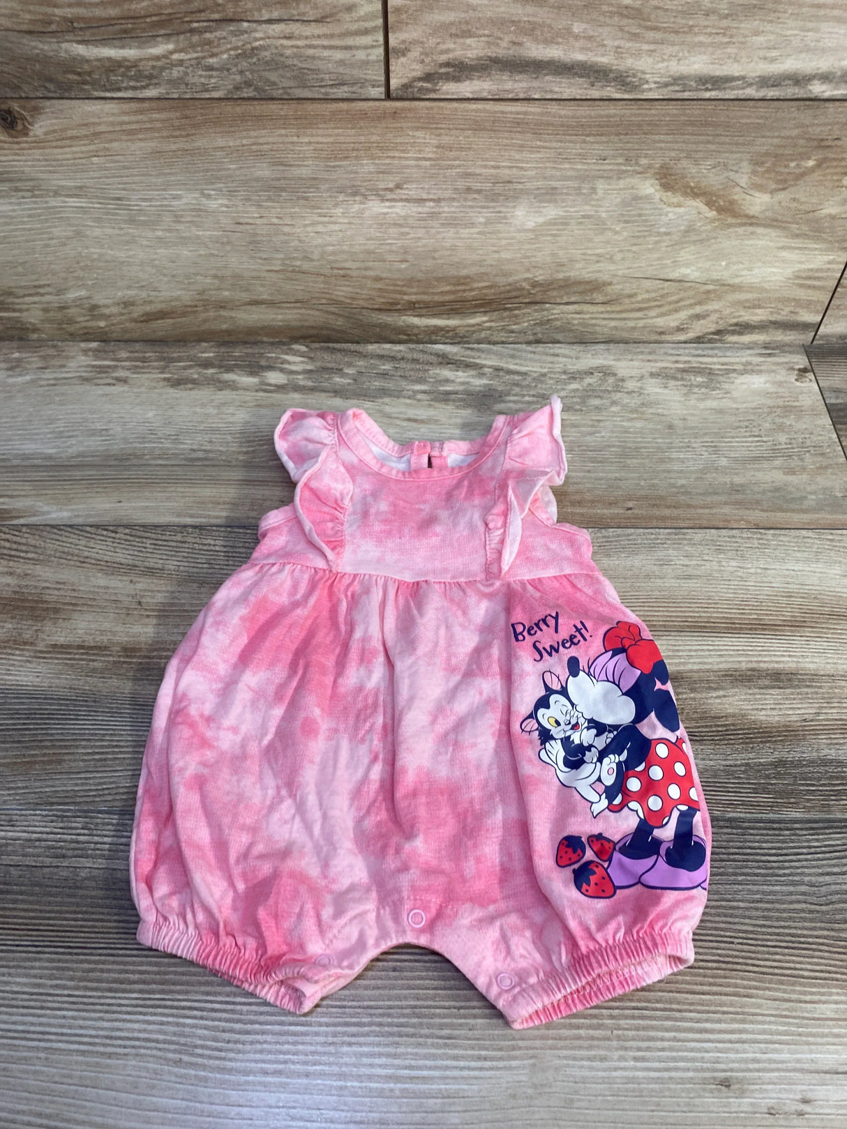 Flat lay of pink Disney Minnie Mouse shortie romper with ruffle sleeves, Berry Sweet print and snap crotch on wood floor