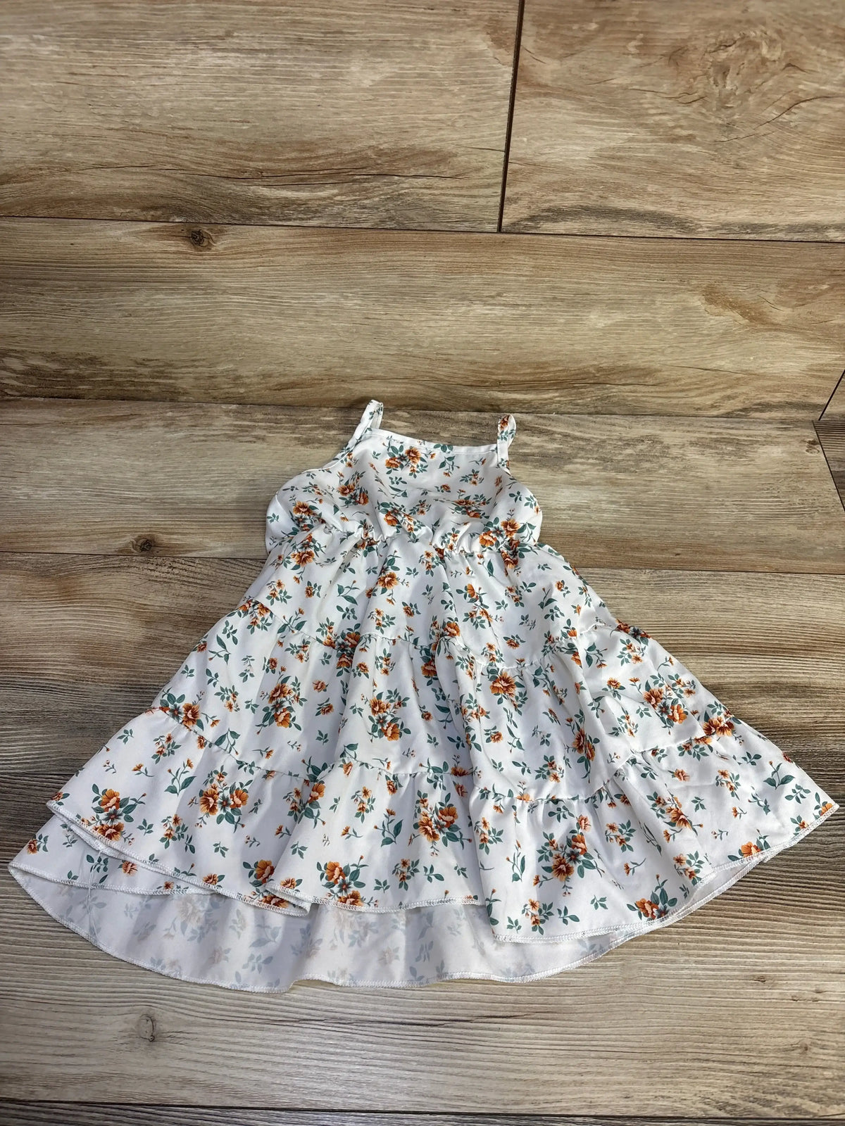 Flat-lay of white tiered toddler dress with orange floral print and ruffled three-tier skirt on wood background