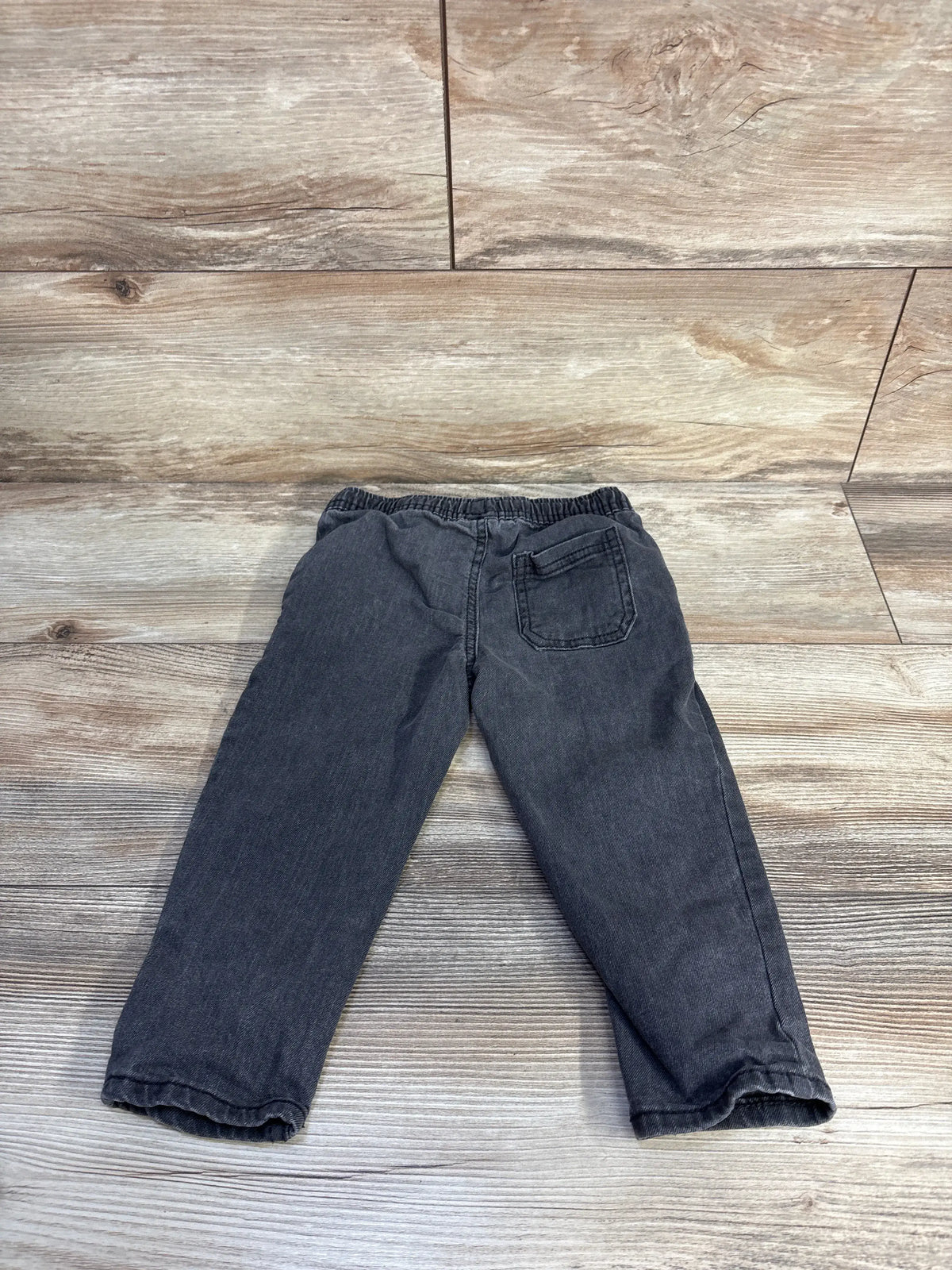 Front view of OshKosh grey drawstring jeans in size 24 months showcasing the adjustable waist and pocket on wood-look flooring